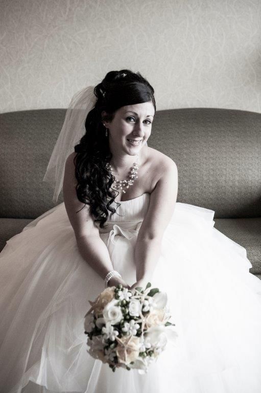 A bride in a wedding dress is sitting on a couch holding a bouquet of flowers.