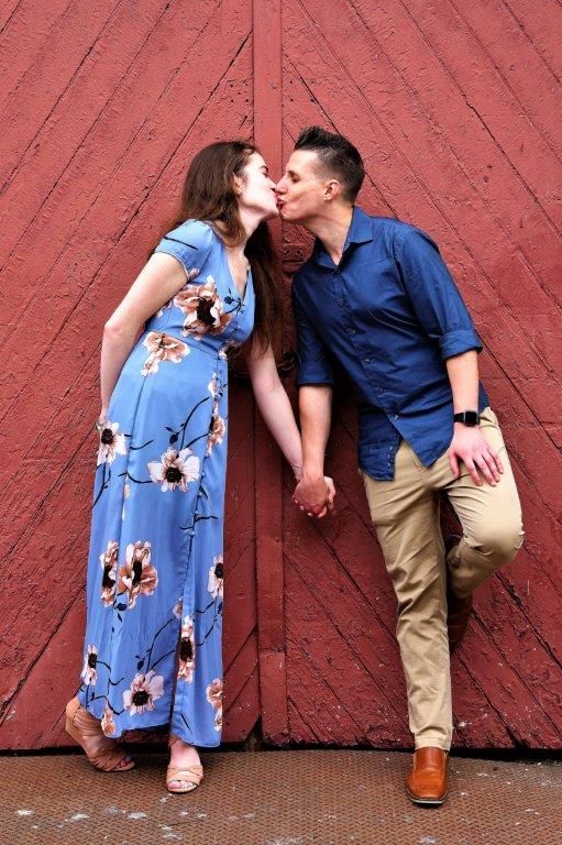 A man and a woman are kissing in front of a red door.