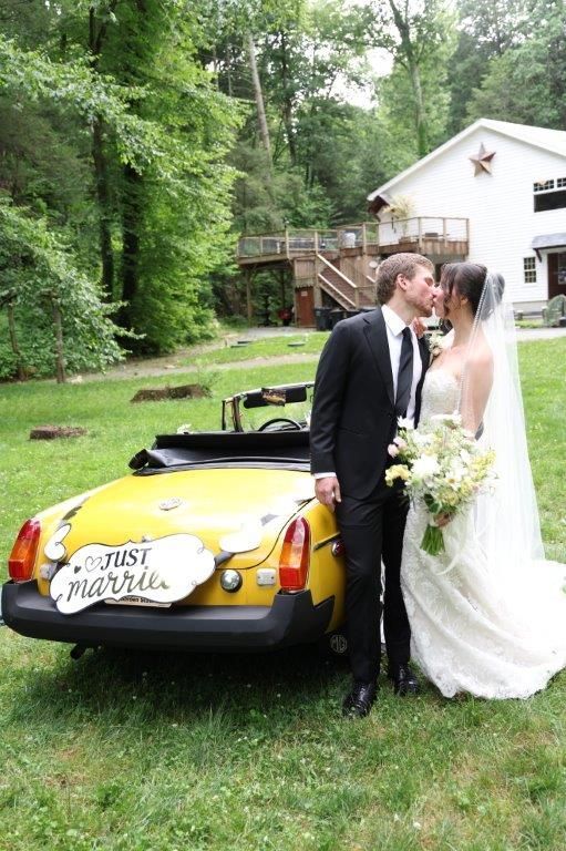 A bride and groom kissing in front of a yellow car that says just married