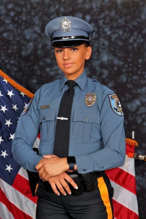 A woman in a police uniform stands in front of an american flag