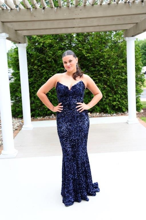 A woman in a blue dress is standing under a pergola with her hands on her hips.