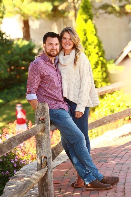 A man and a woman are posing for a picture while leaning on a wooden fence.