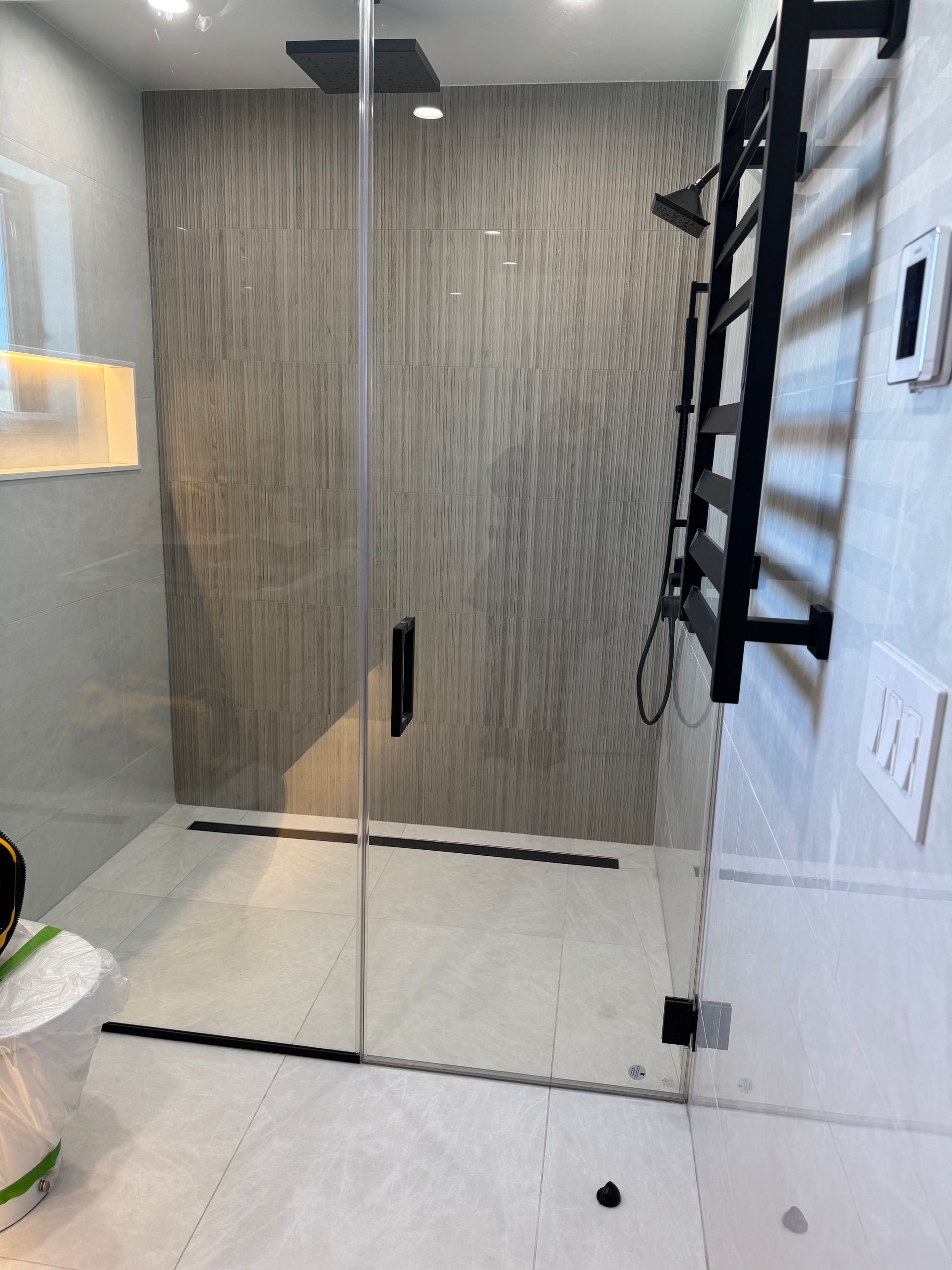 A modern walk-in shower with a glass door, textured gray accent wall, black hardware, and an integrated drain.