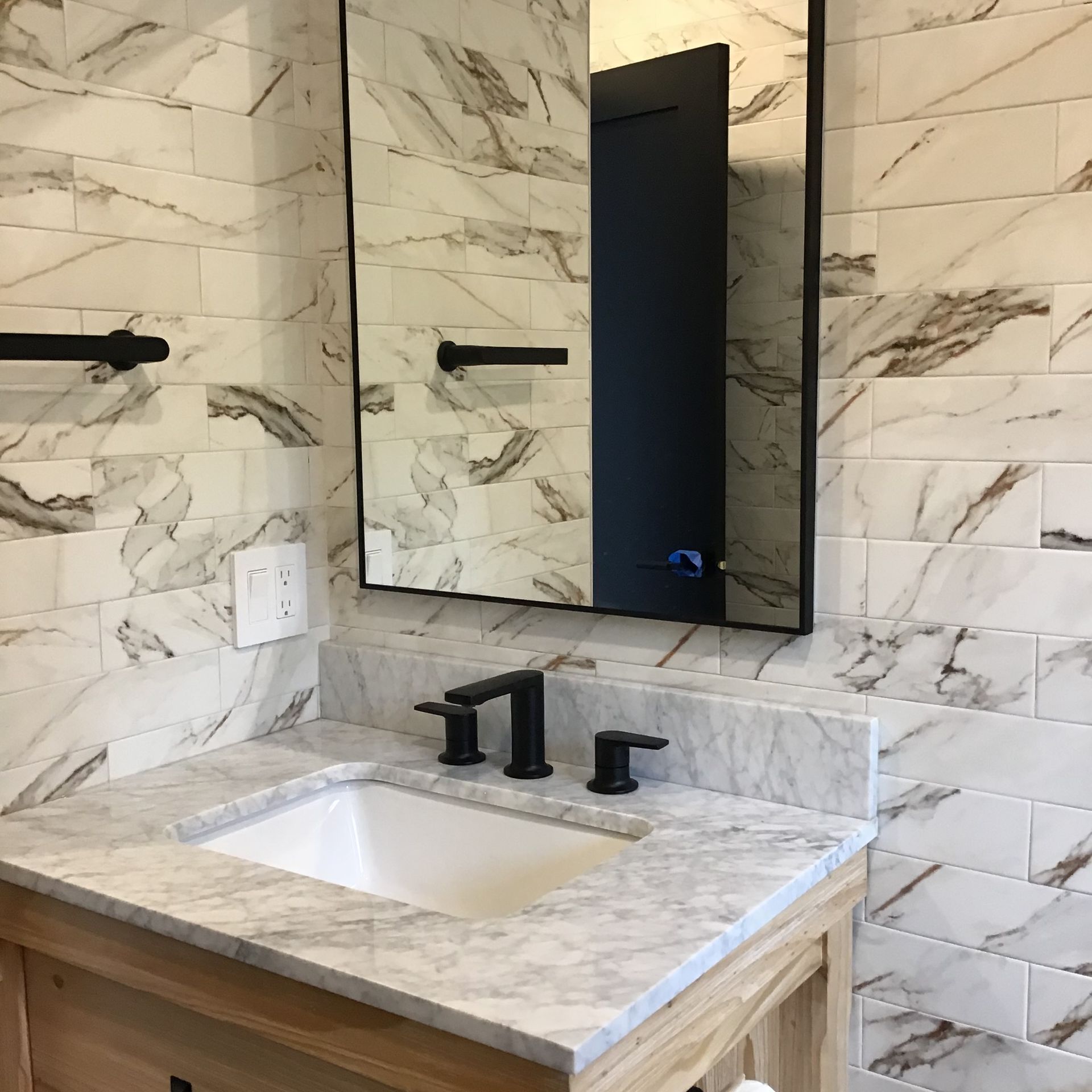 Marble bathroom vanity with black faucet, rectangular sink, and wall mirror in a tiled room