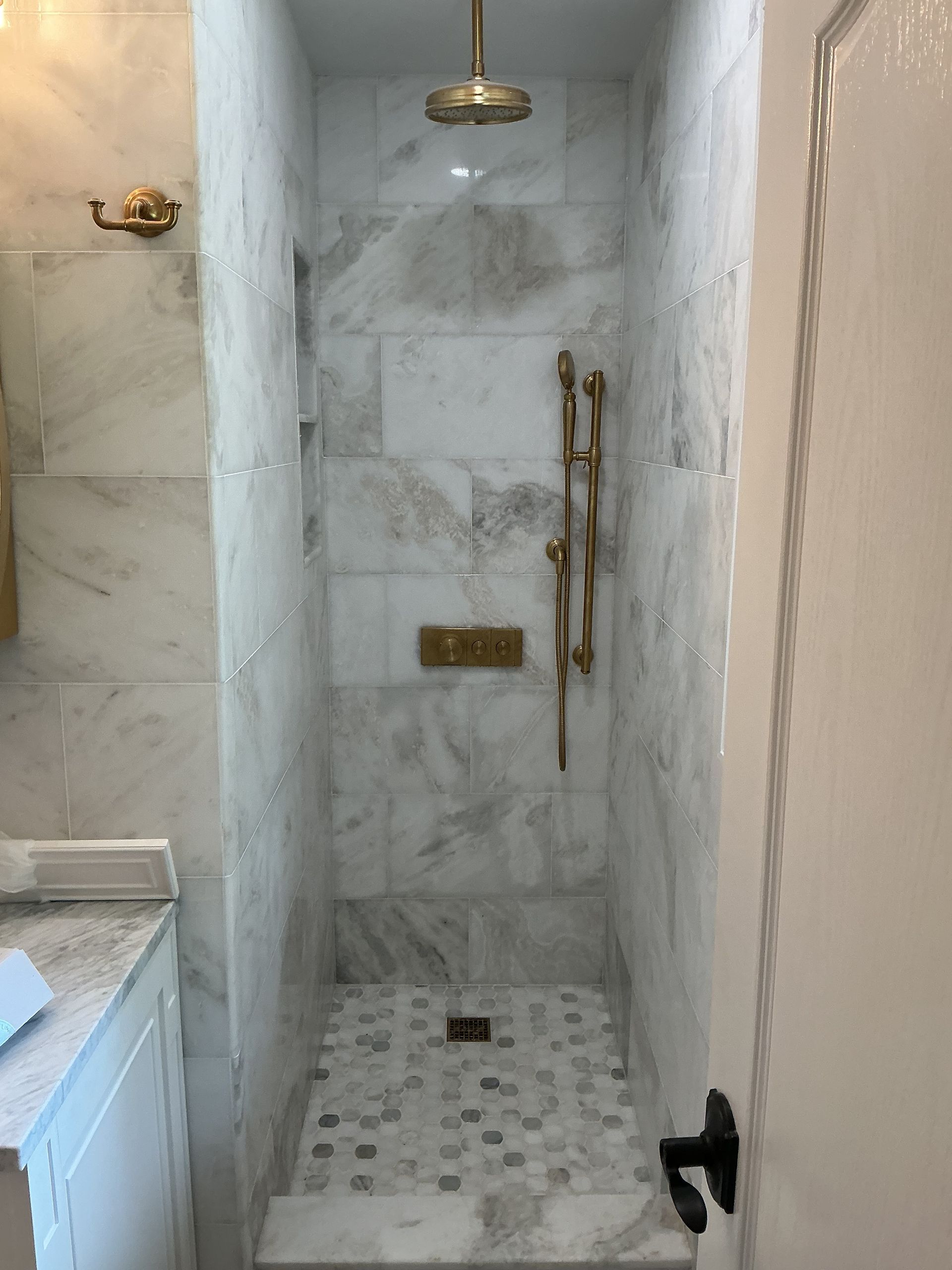 Marble-tiled walk-in shower with brass fixtures and mosaic floor in a bathroom