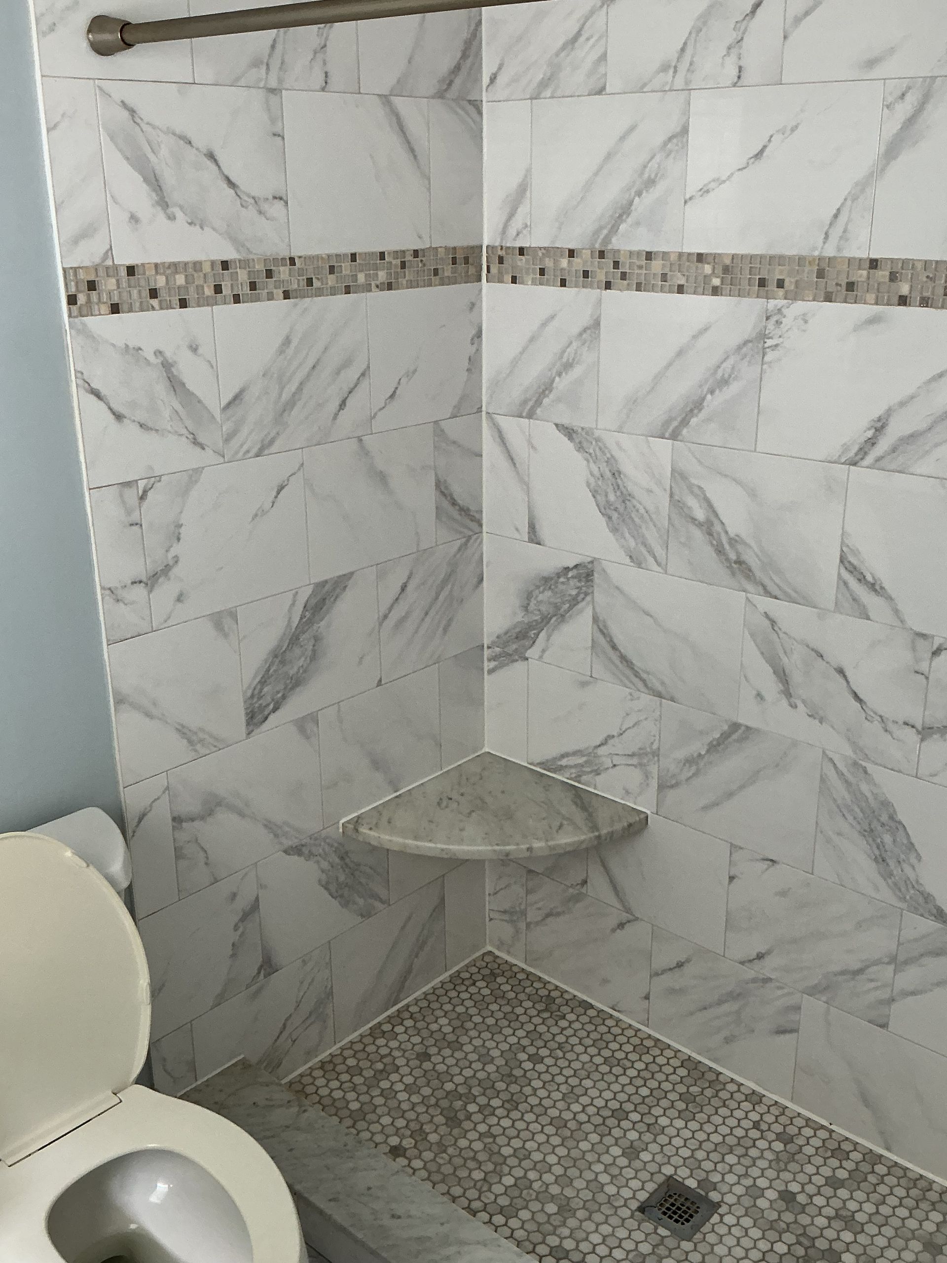 Corner shower with gray marble-look tile, pebble shower floor, and a built-in corner shelf.