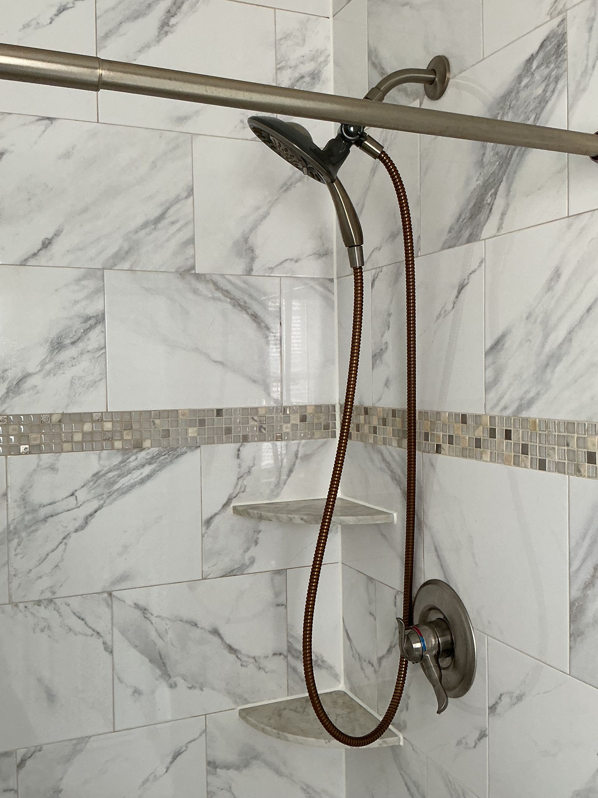 Shower stall with marble-look tile and a handheld showerhead on a hose