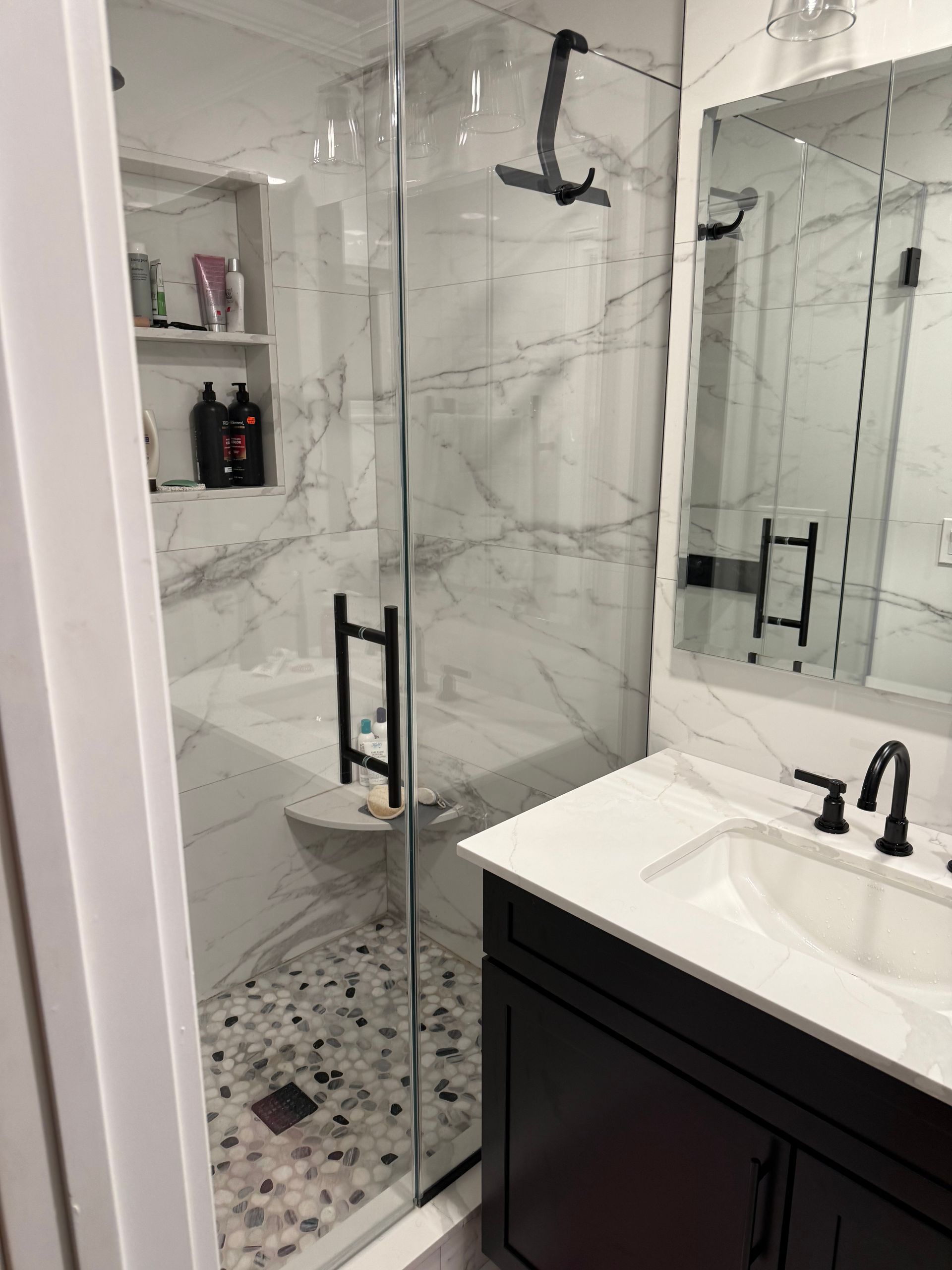 Modern bathroom with glass shower, black fixtures, white marble walls, and black vanity with sink and mirror