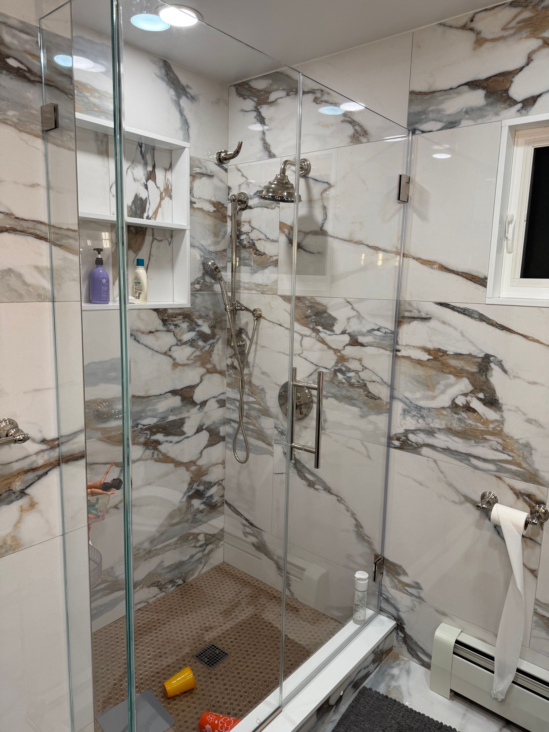 Modern bathroom with marble-pattern tile, glass shower enclosure, and a small window over the shower.