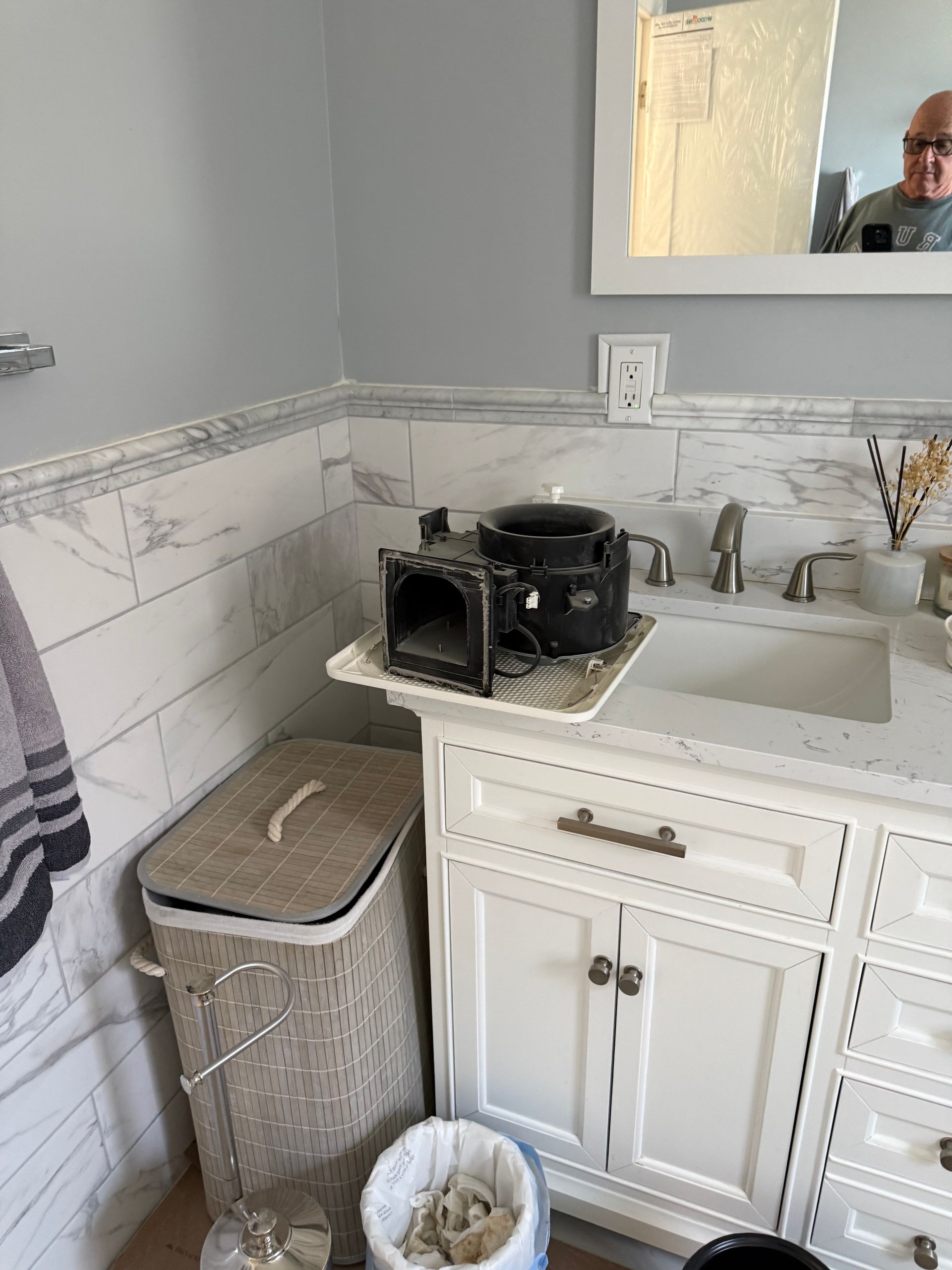 Bathroom vanity with white cabinets, mirror, sink, and countertop items beside a wicker laundry hamper.