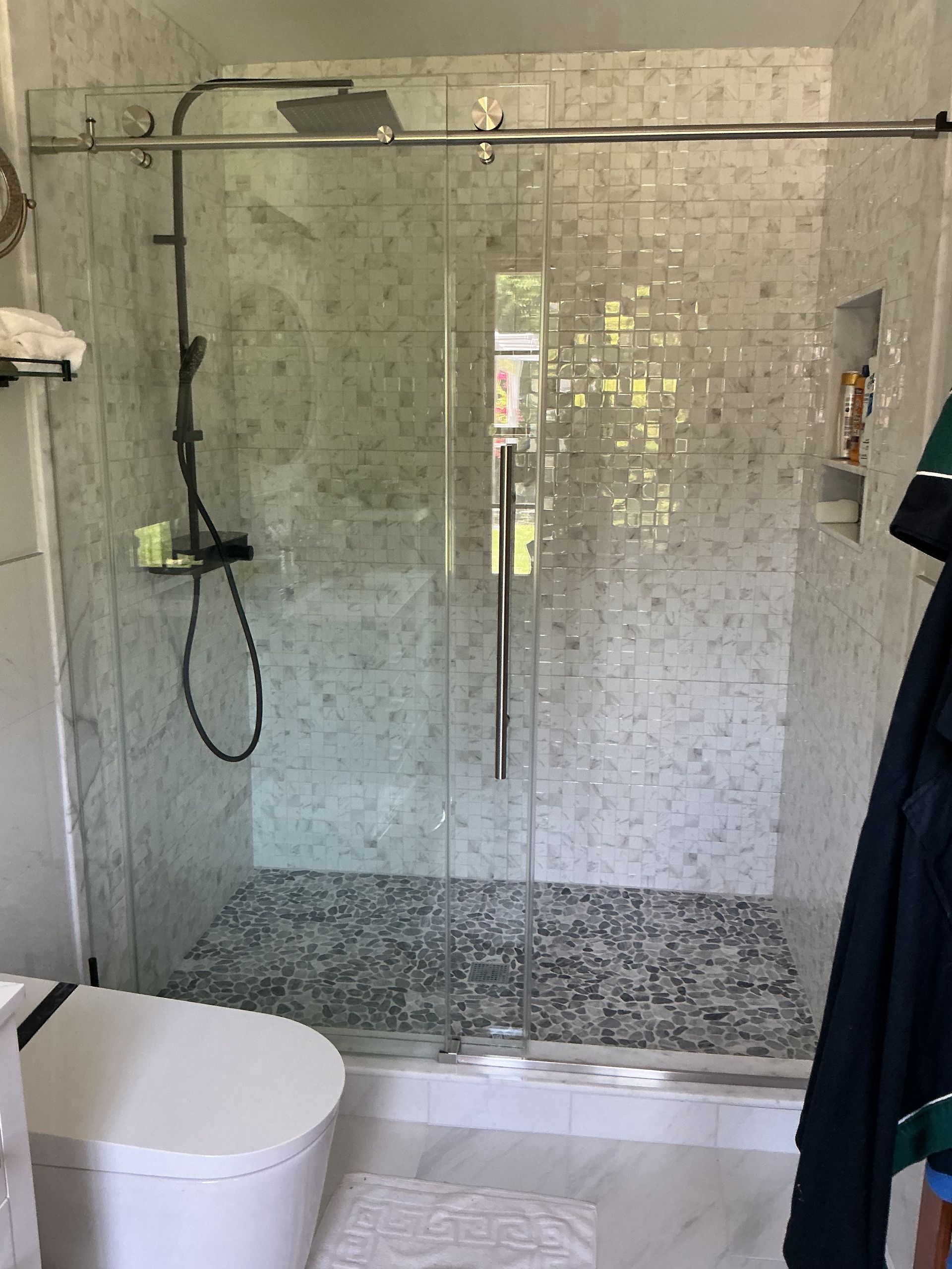 Bathroom with glass walk-in shower, mosaic tile wall, and white toilet in the foreground