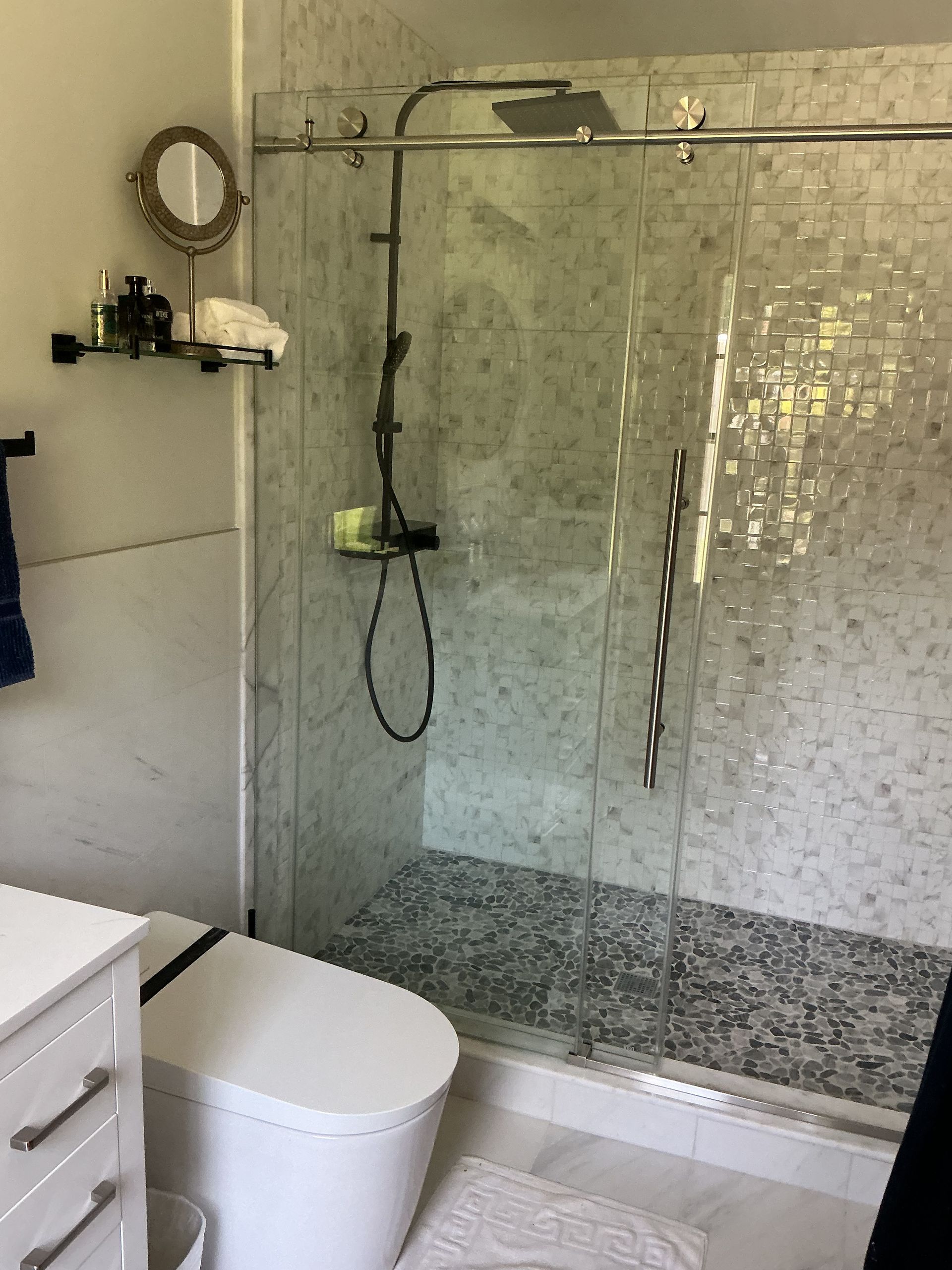 Modern bathroom with glass shower, tiled walls, and white toilet beside a sink.