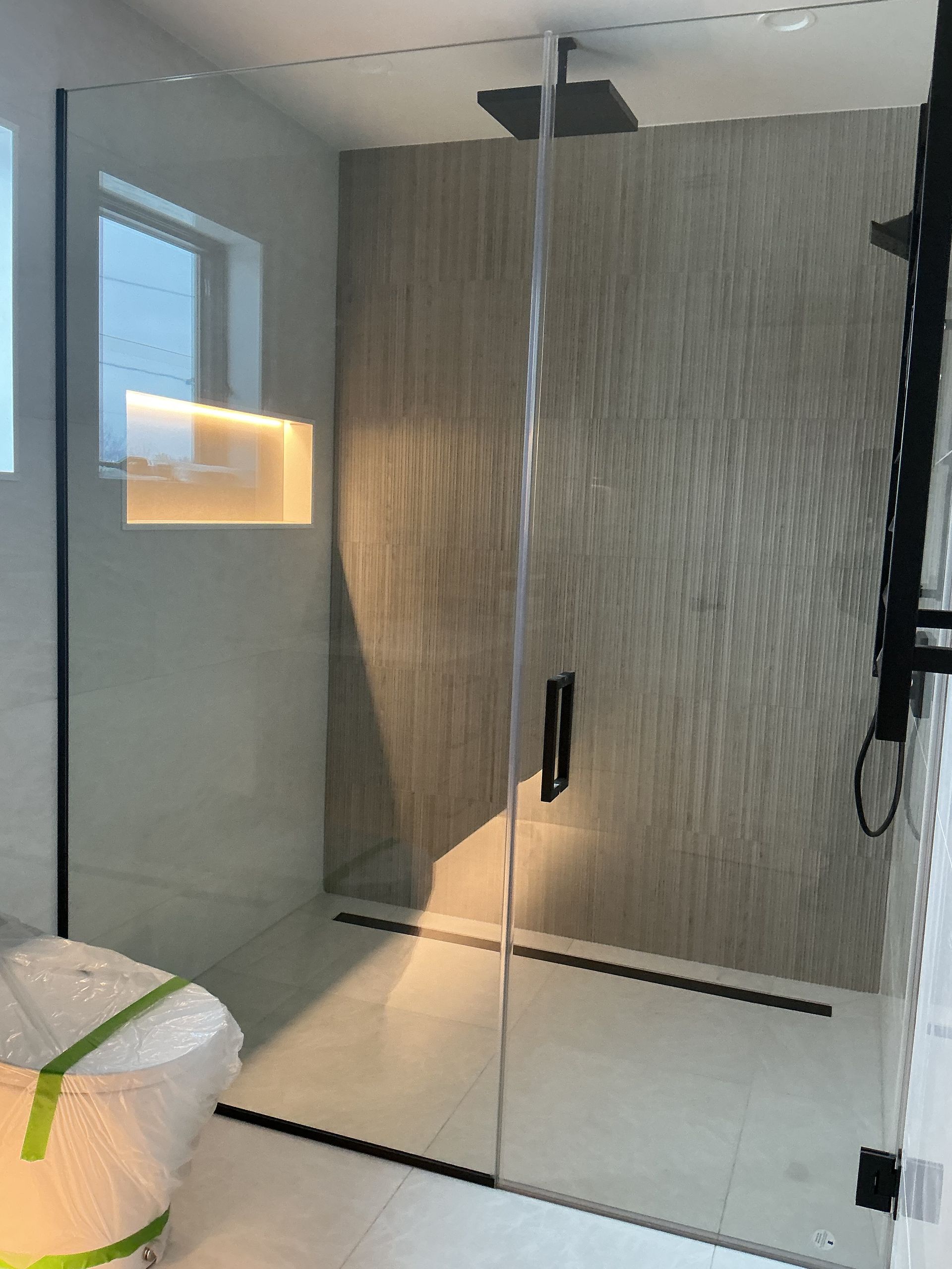 Modern bathroom with glass shower enclosure, black handle, and white tiled walls.