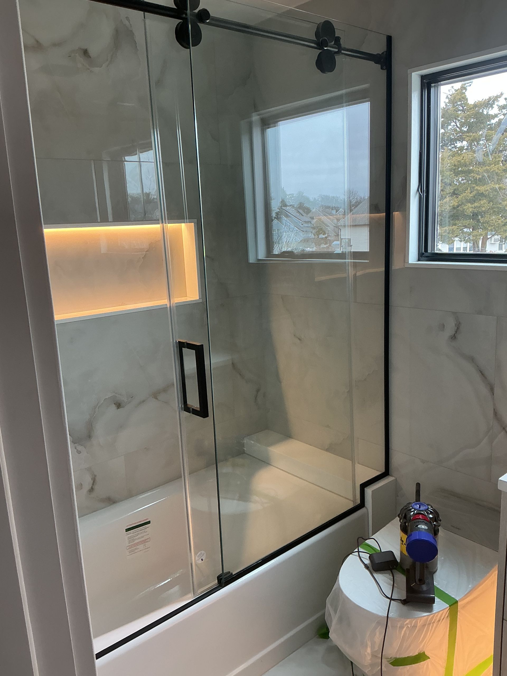 Modern bathroom with glass shower enclosure, marble walls, window, and a round sink with toiletries.