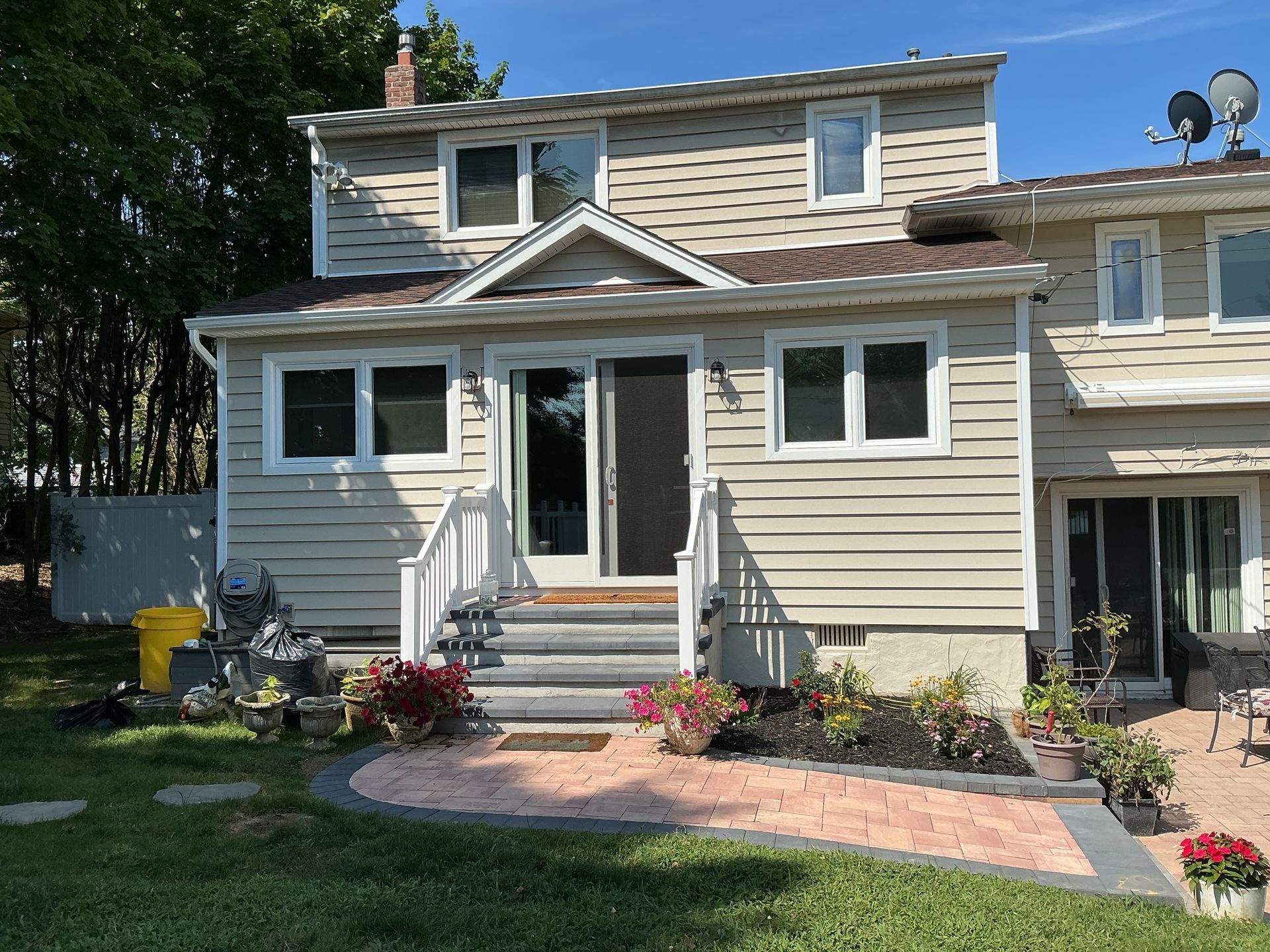 Two-story beige house with front steps, flower beds, and a brick walkway in daylight