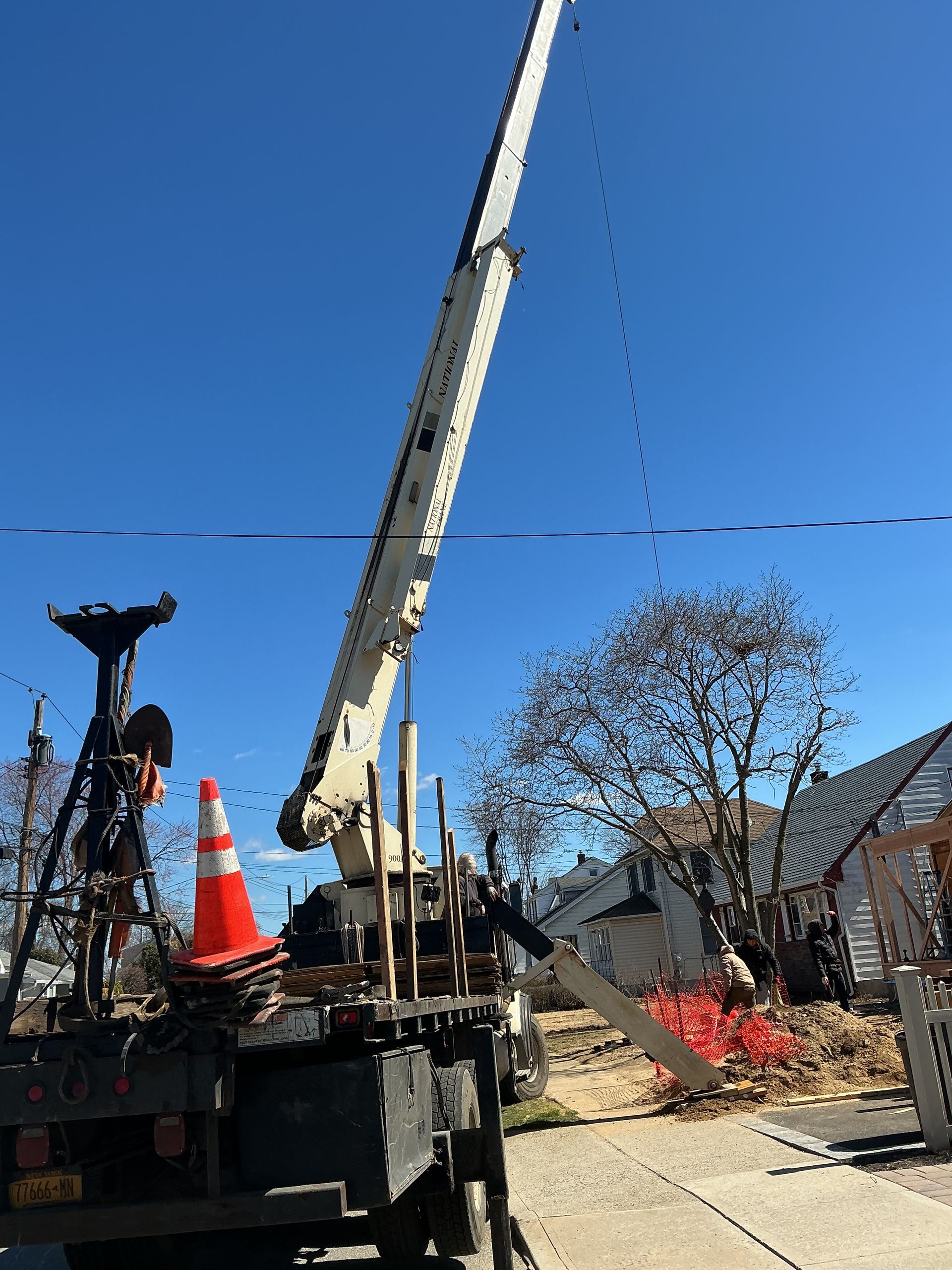 Construction crane lifting debris beside an orange cone under a clear blue sky.
