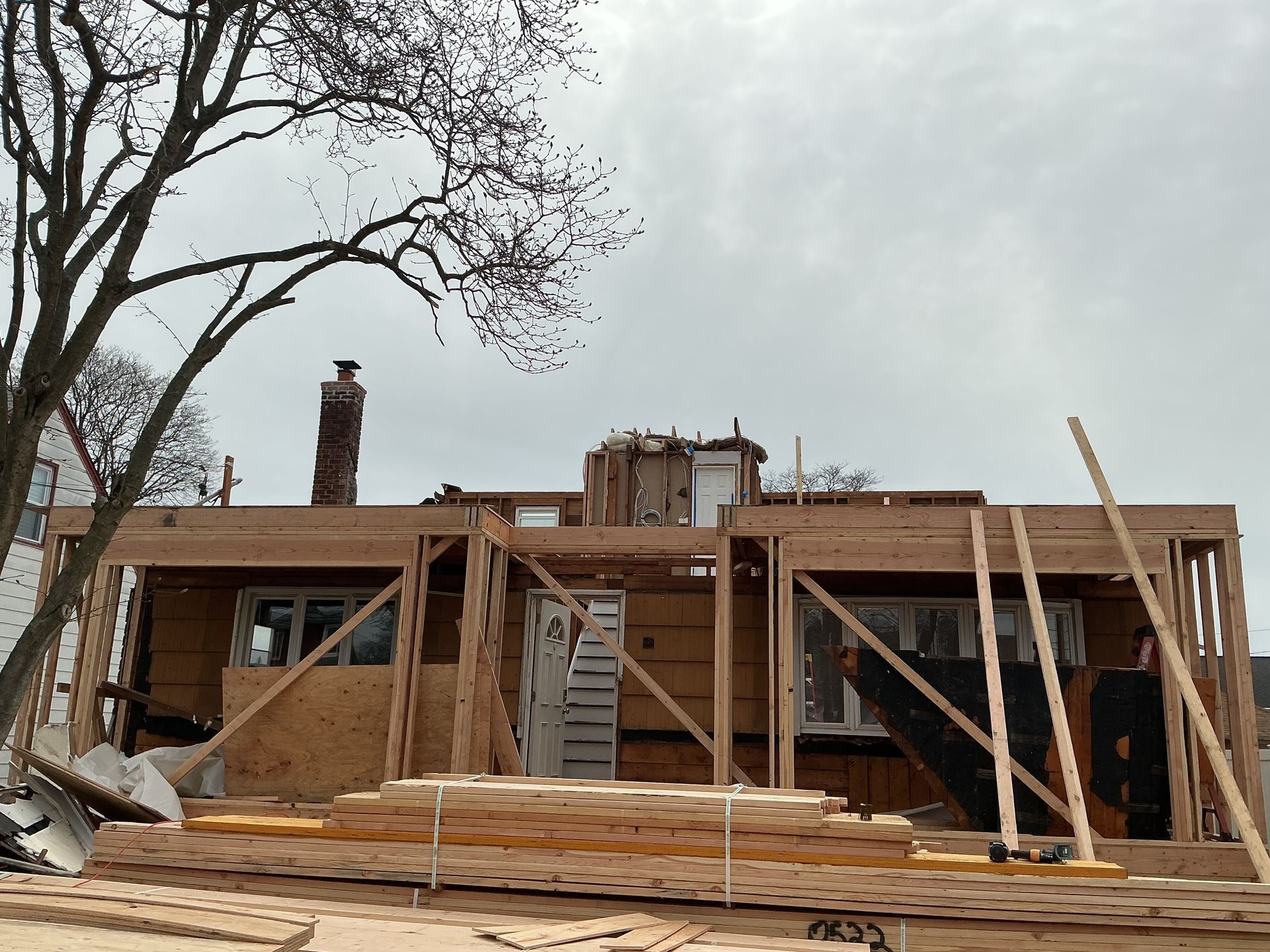 Partially built wooden house under construction with scaffolding and stacked lumber under a gray sky