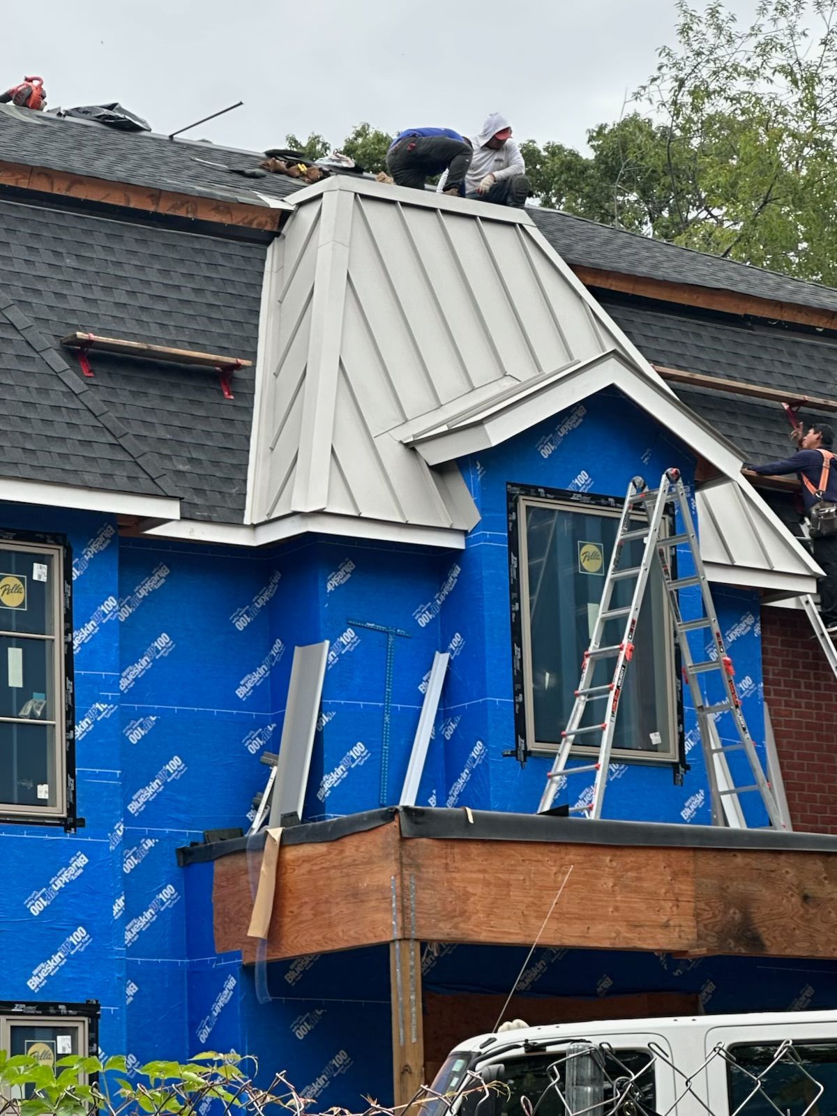 Workers installing siding and roofing on a house with scaffolding and ladders