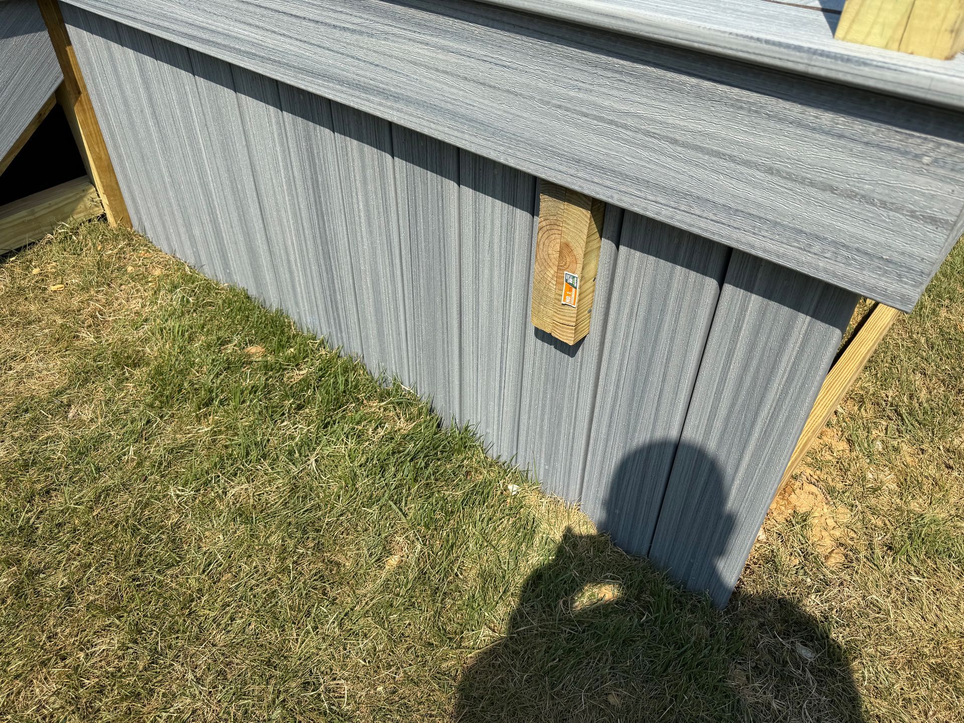 Gray shed wall with a small wooden patch, beside grass in sunlight