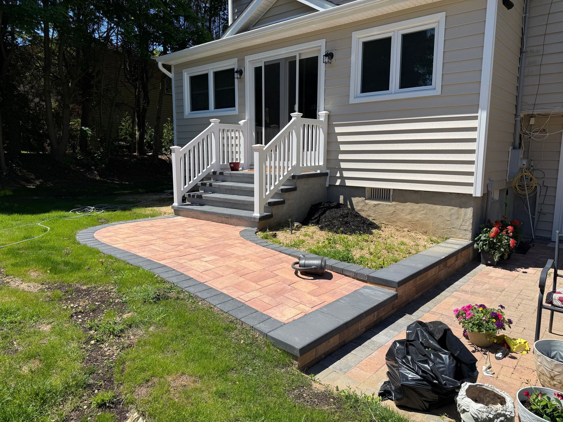 Front porch with white railing, brick walkway, and potted flowers beside a house.