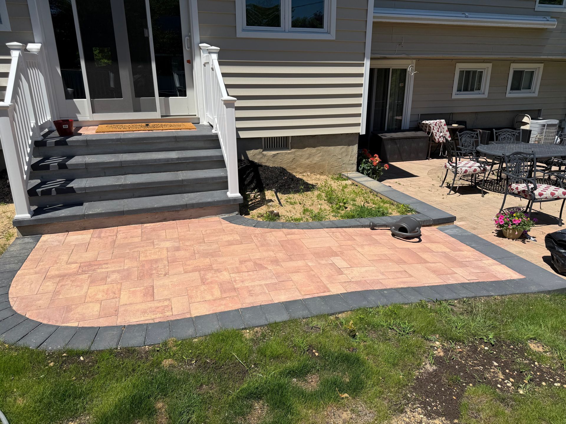 Front porch steps beside a brick patio and garden beds outside a beige house