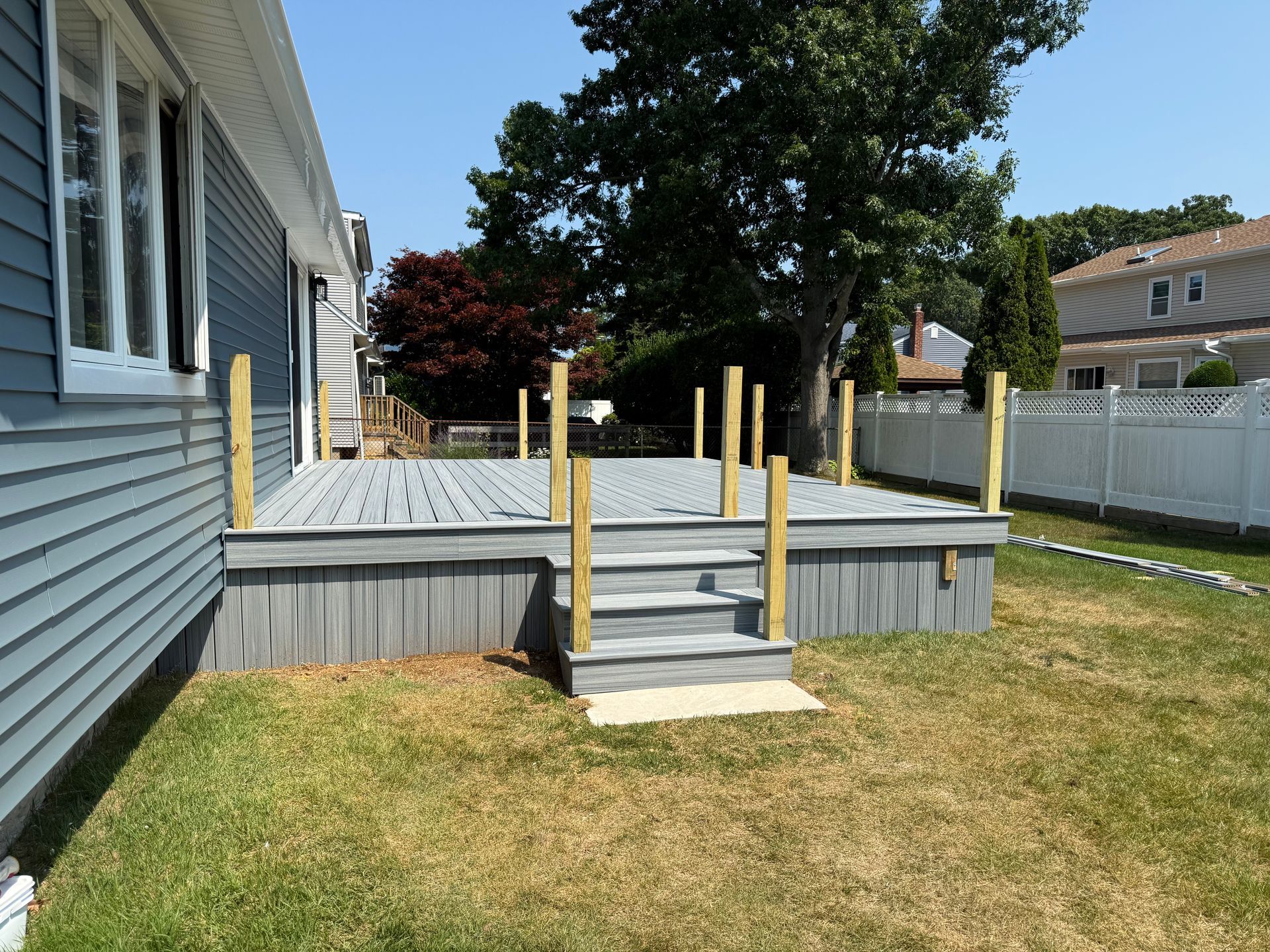 Backyard deck with gray steps, white railing posts, and a house beside a grassy lawn