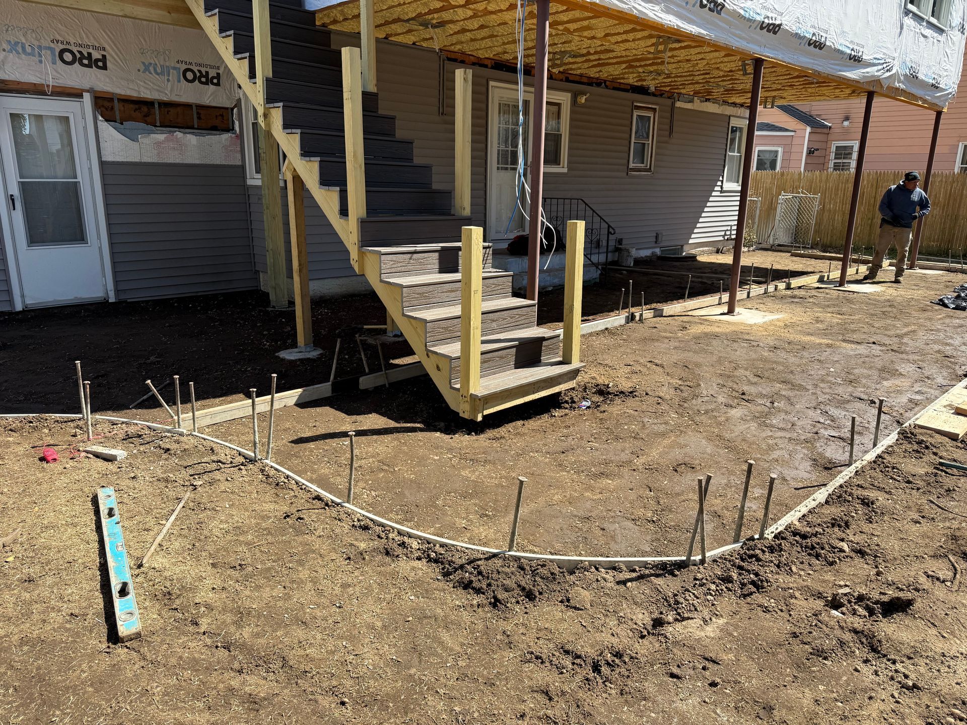 Exterior of a raised house with stairs and a partially dug foundation area in the foreground