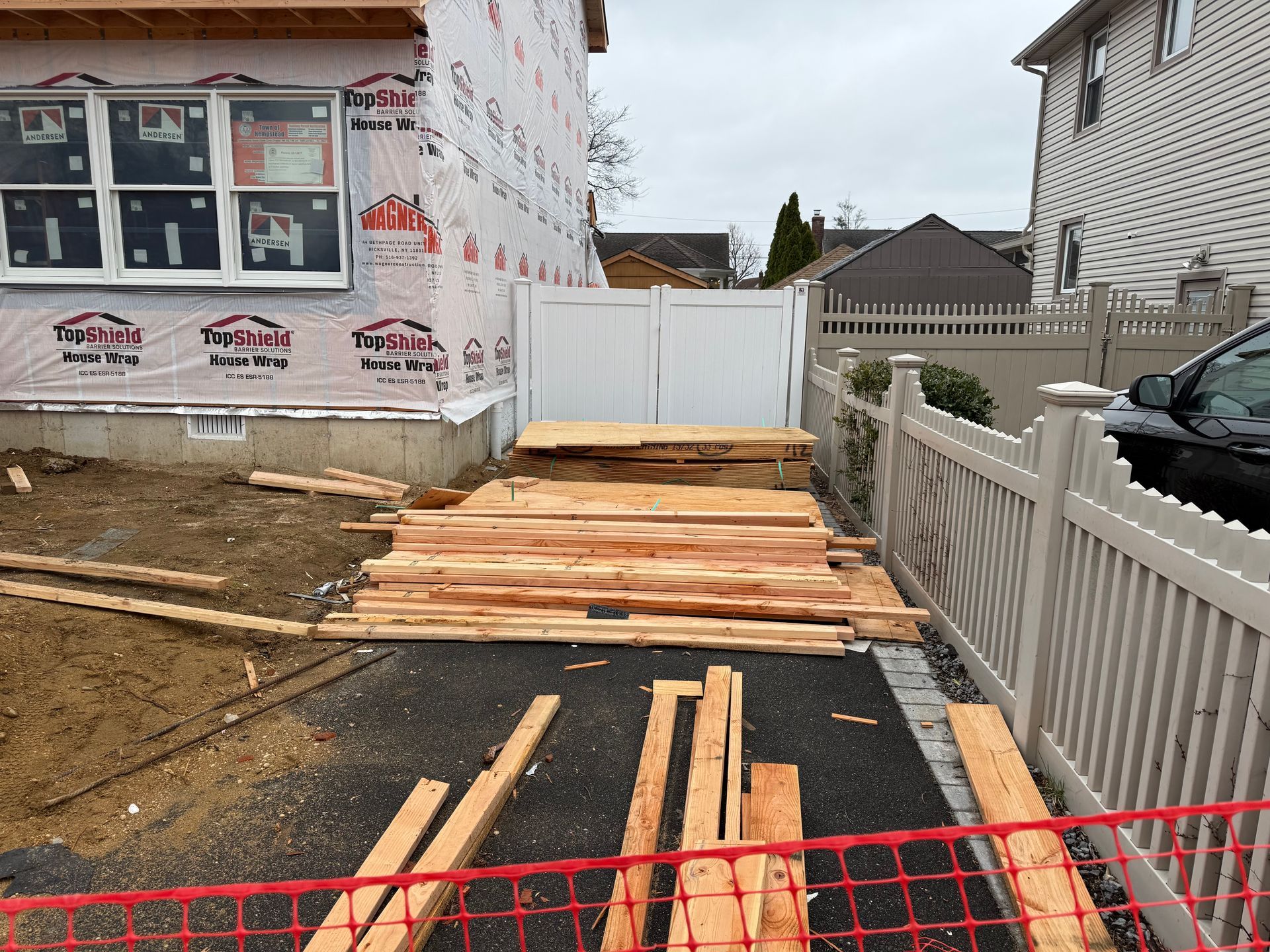 Wooden planks and boards laid across a driveway under construction beside a house and white fence