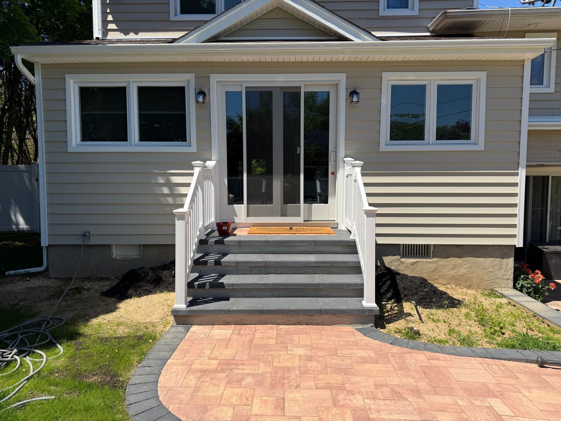 Front entrance of a house with steps, white railings, and a brick walkway leading to double doors