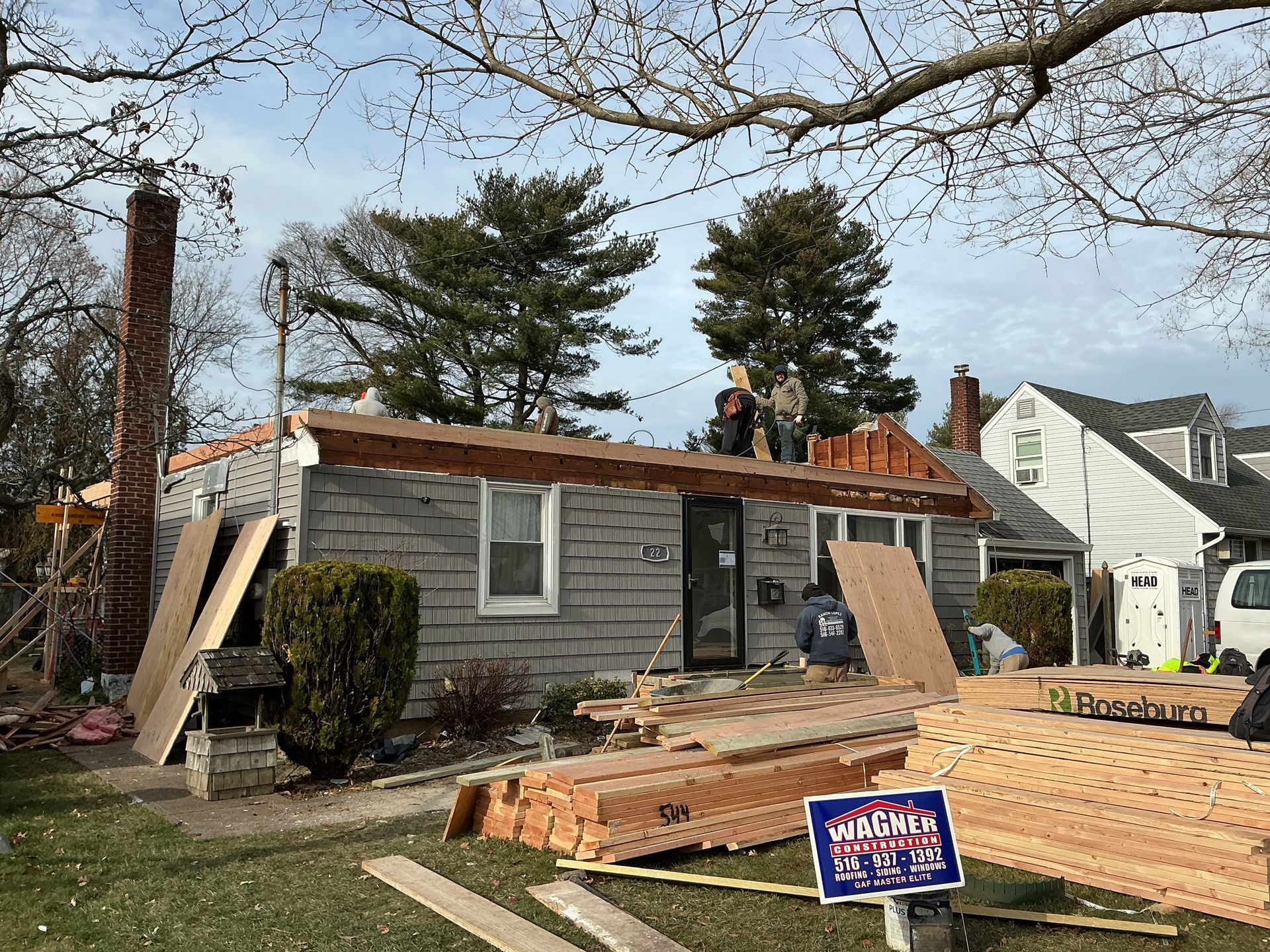 Roof under construction on a house, with lumber, ladders, and workers on top.