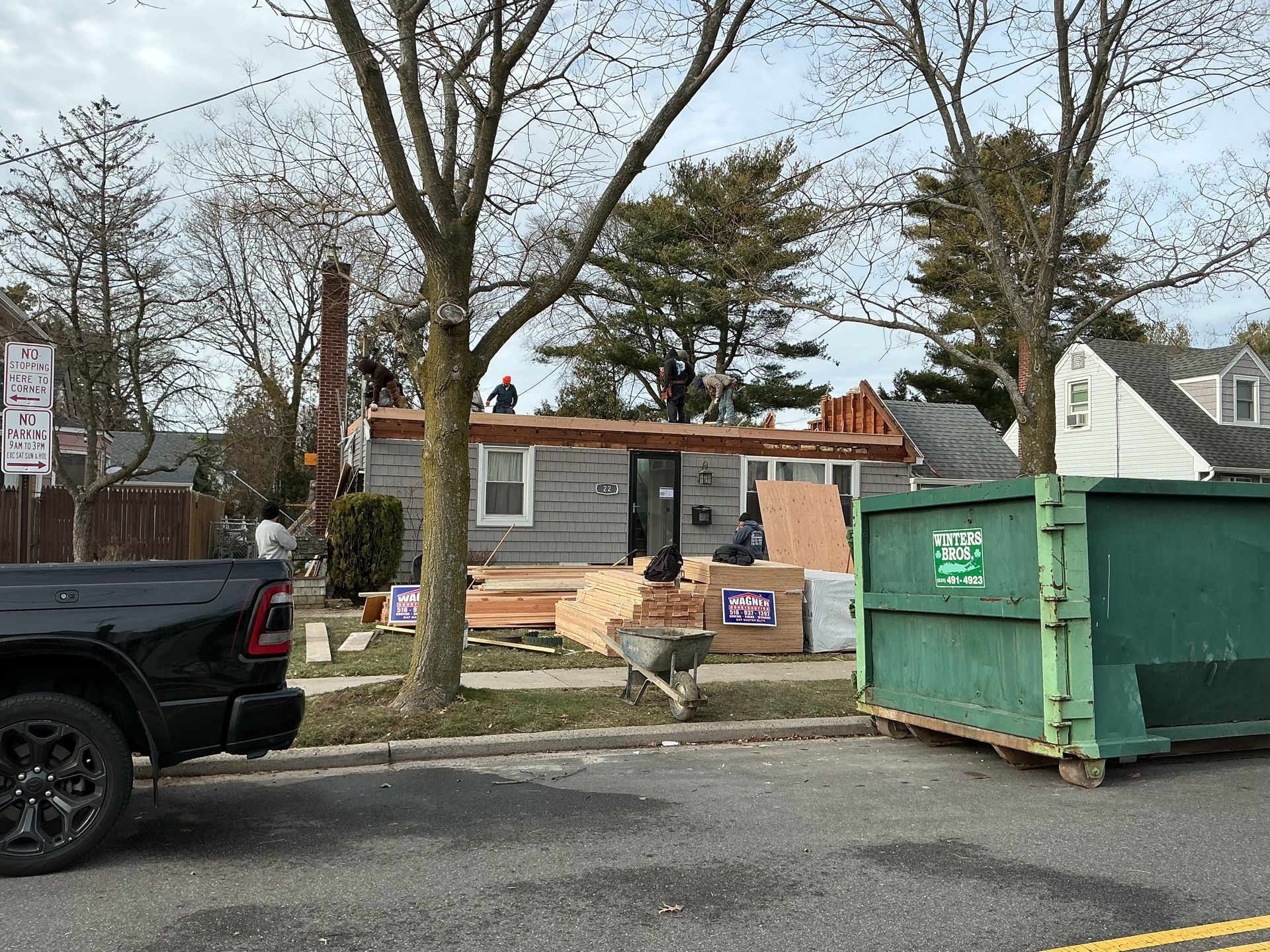 Residential house under construction with a green dumpster in front and a pickup truck parked nearby.