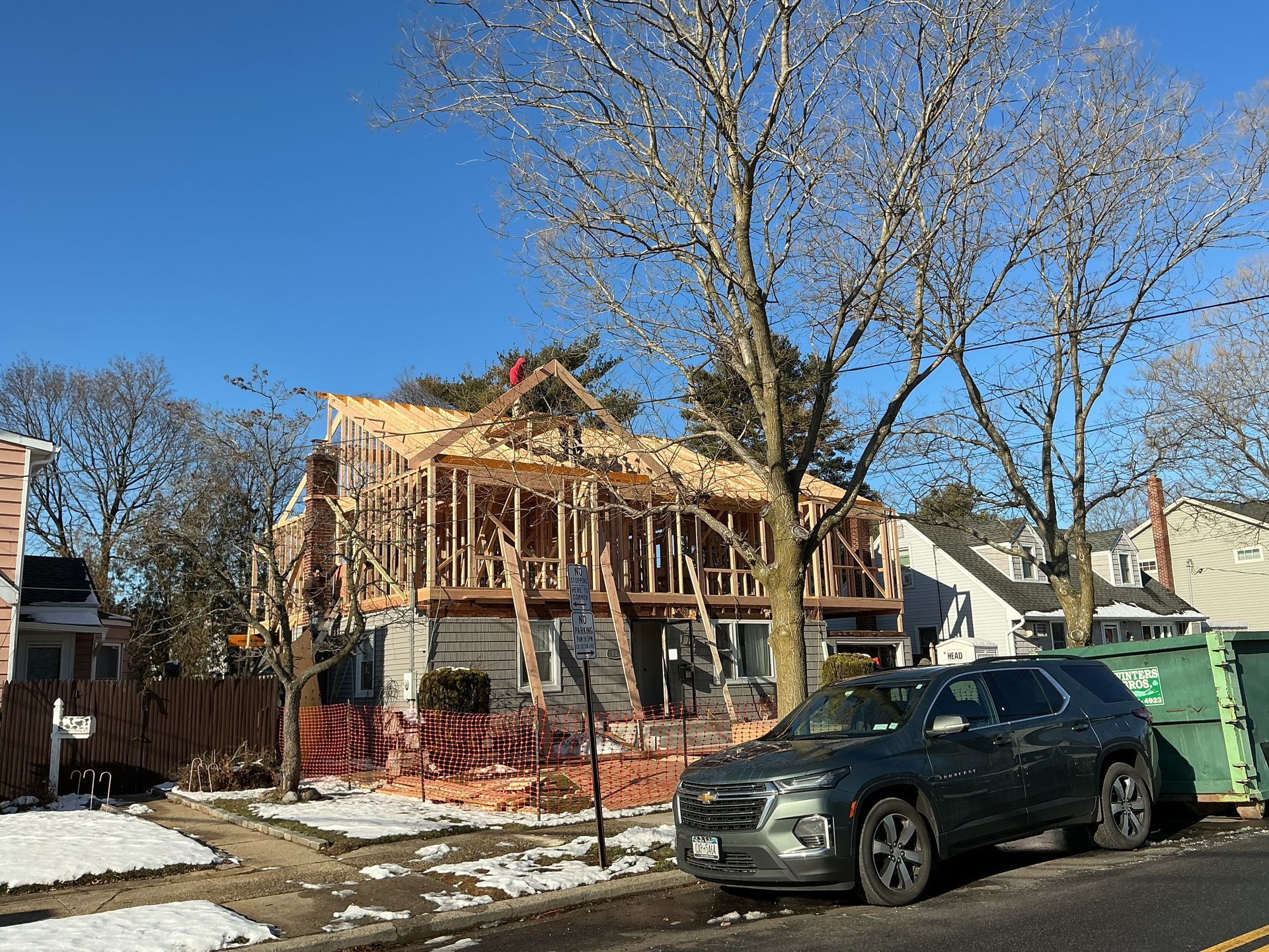 Partially demolished house under construction with exposed framing, black SUV parked in front, and bare winter trees