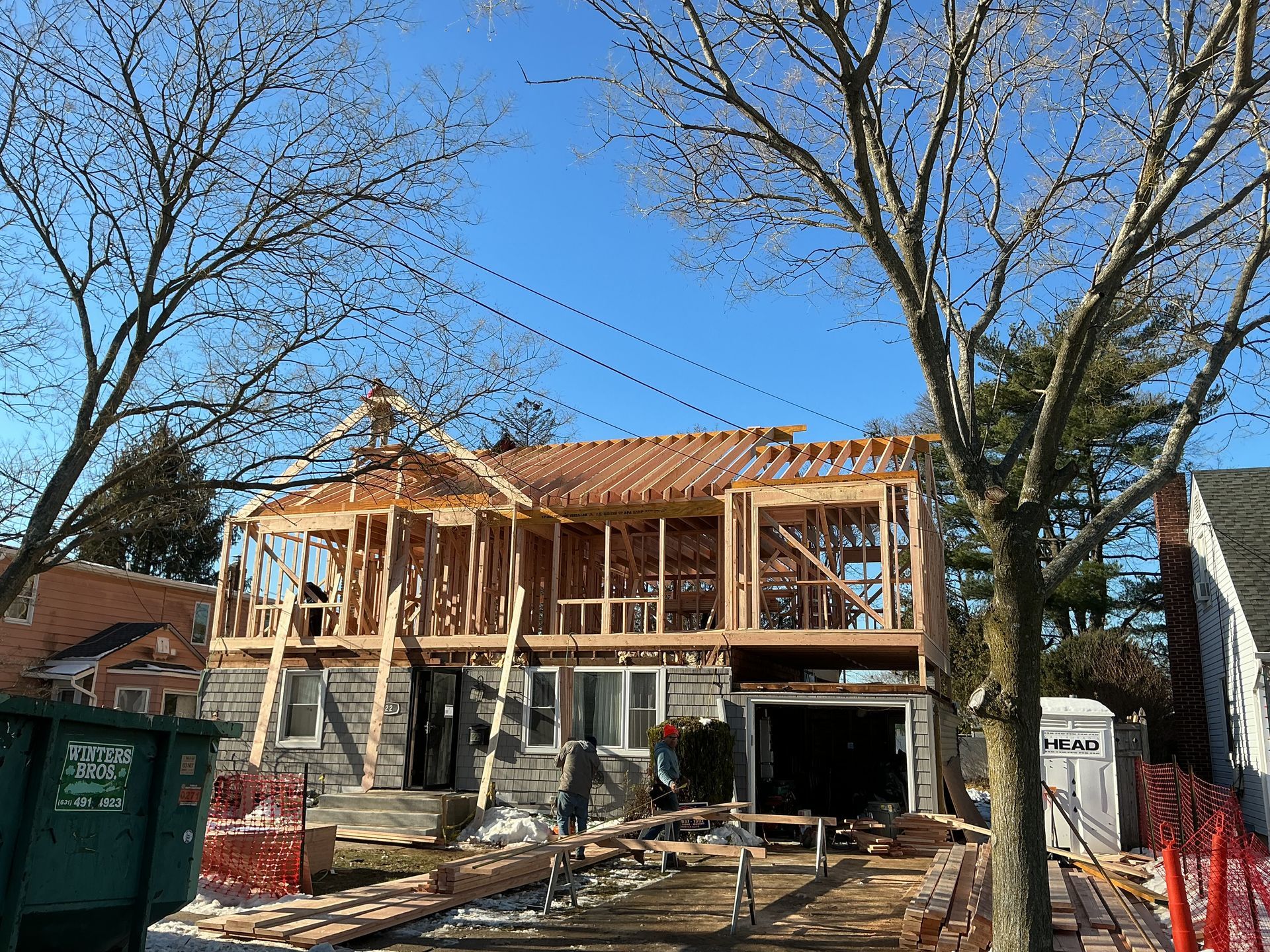 House under construction with exposed framing, scaffolding, and a large tree in front