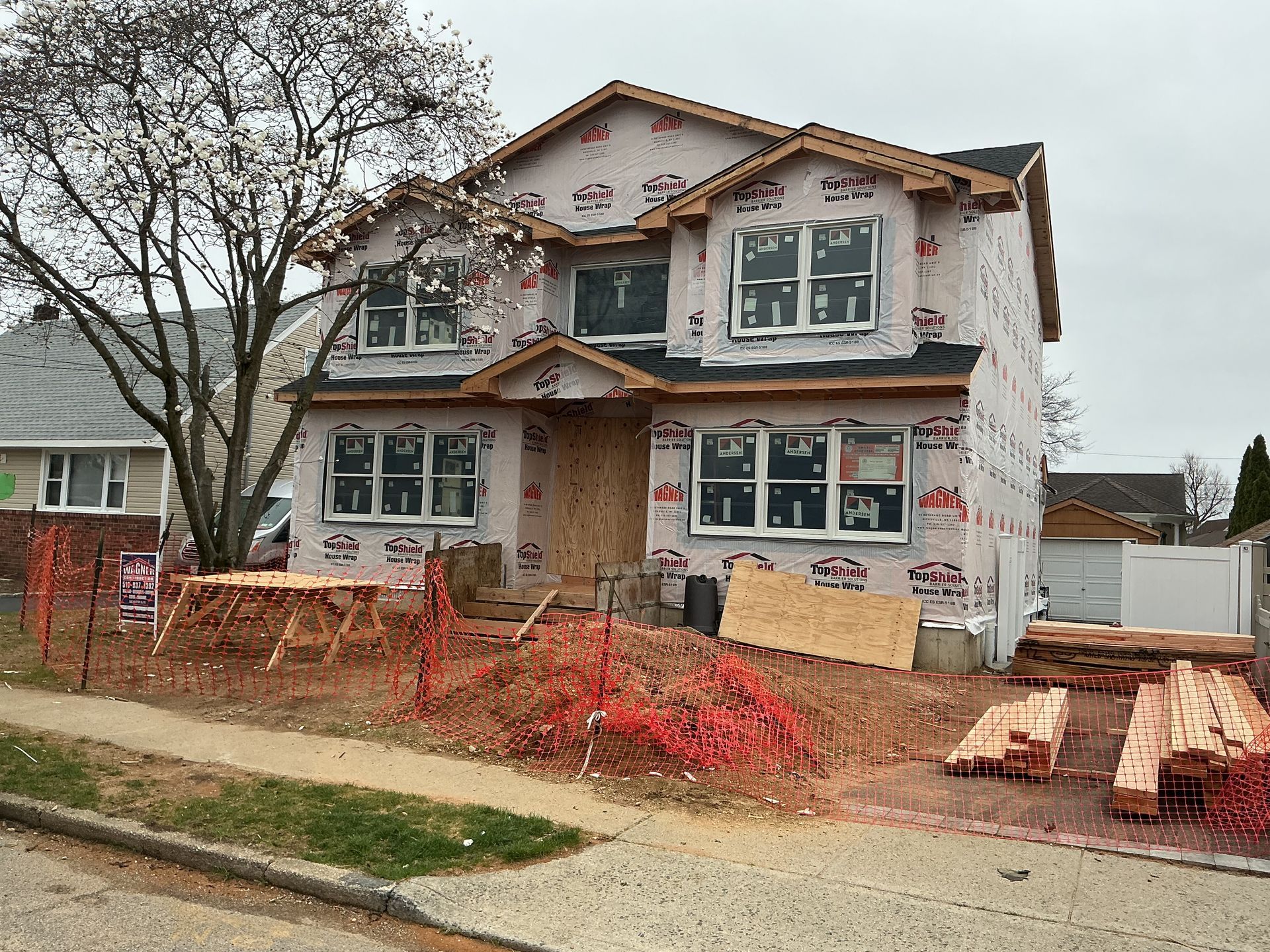 Two-story house under construction with exposed insulation, framed yard, and a sidewalk in front