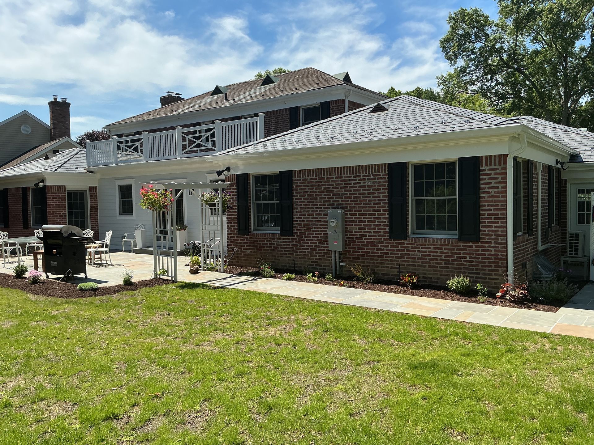 Brick house with metal roof, green shutters, and a covered patio beside a grassy yard