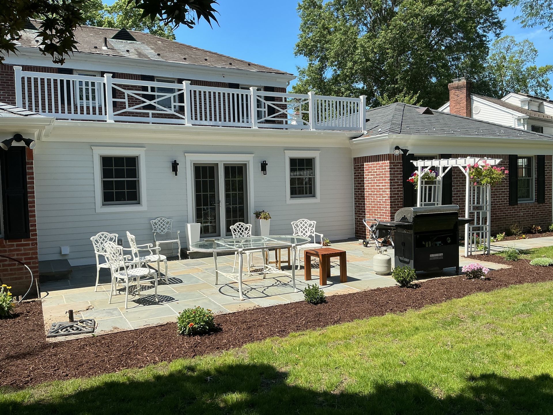 Back patio with white outdoor furniture, grill, and red umbrella beside a house