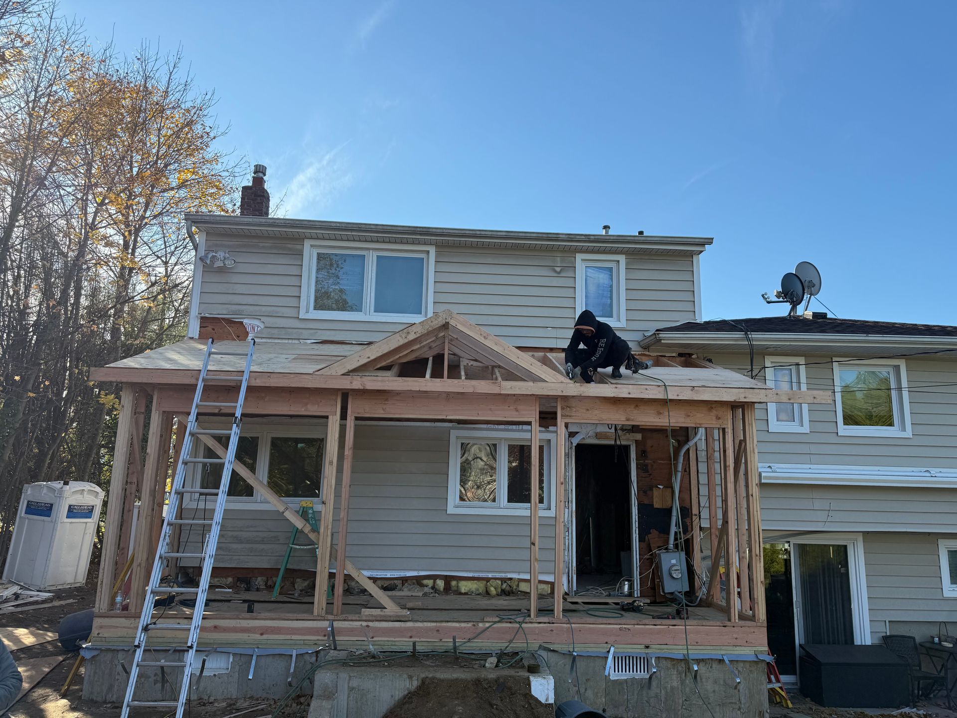 House under construction with a new wooden front porch framing and ladders on the exterior.