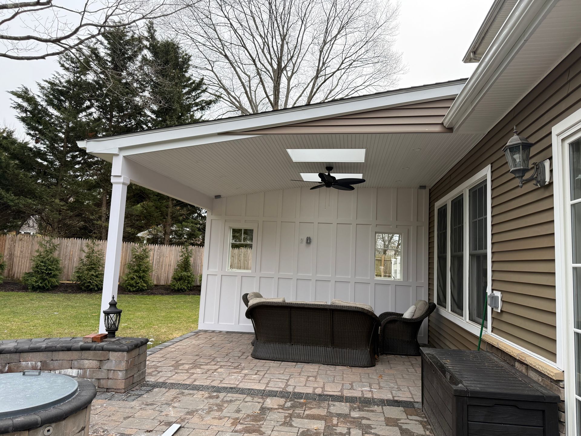 Covered backyard patio with wicker seating, ceiling fan, and white double doors beside the house.
