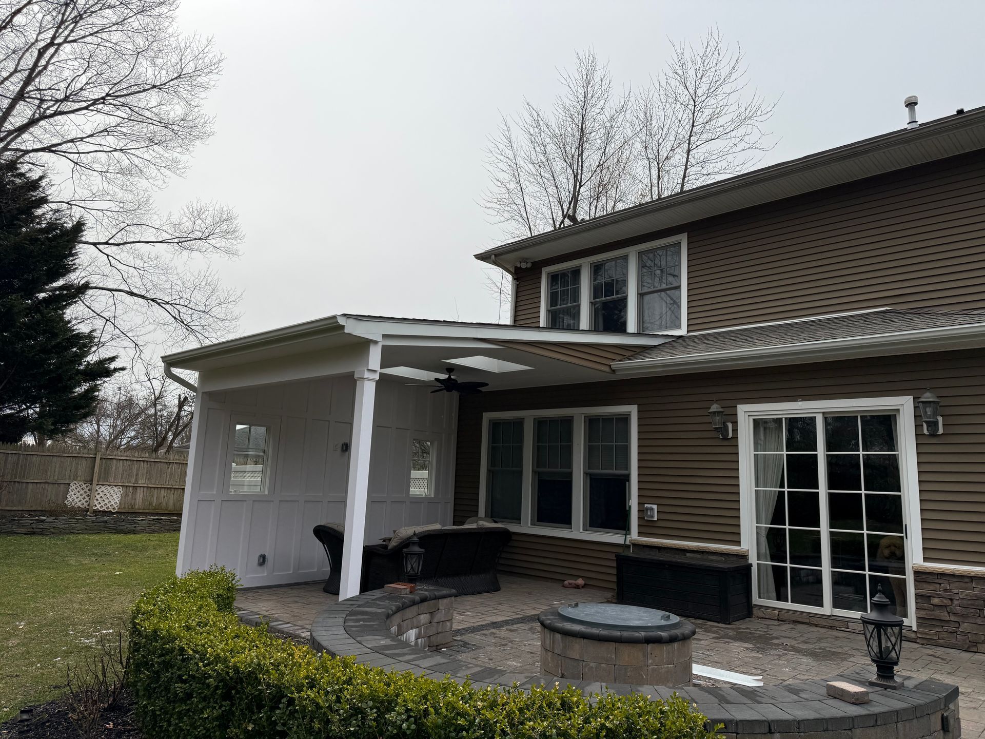 Back patio of a two-story house with a covered porch, brick wall, and patio furniture under an overcast sky