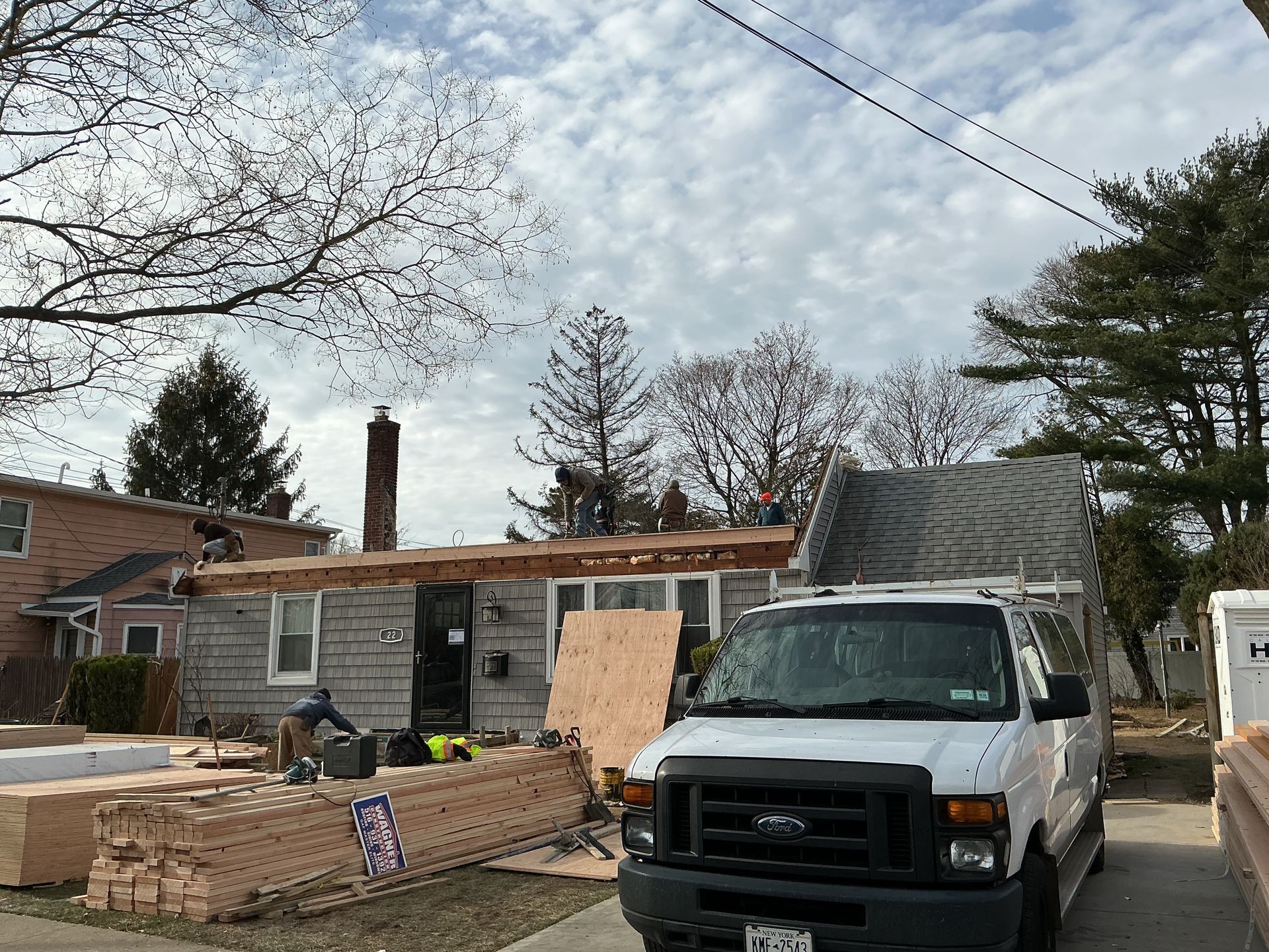 Damaged house with boarded windows and roof repair in progress, white truck parked in front.