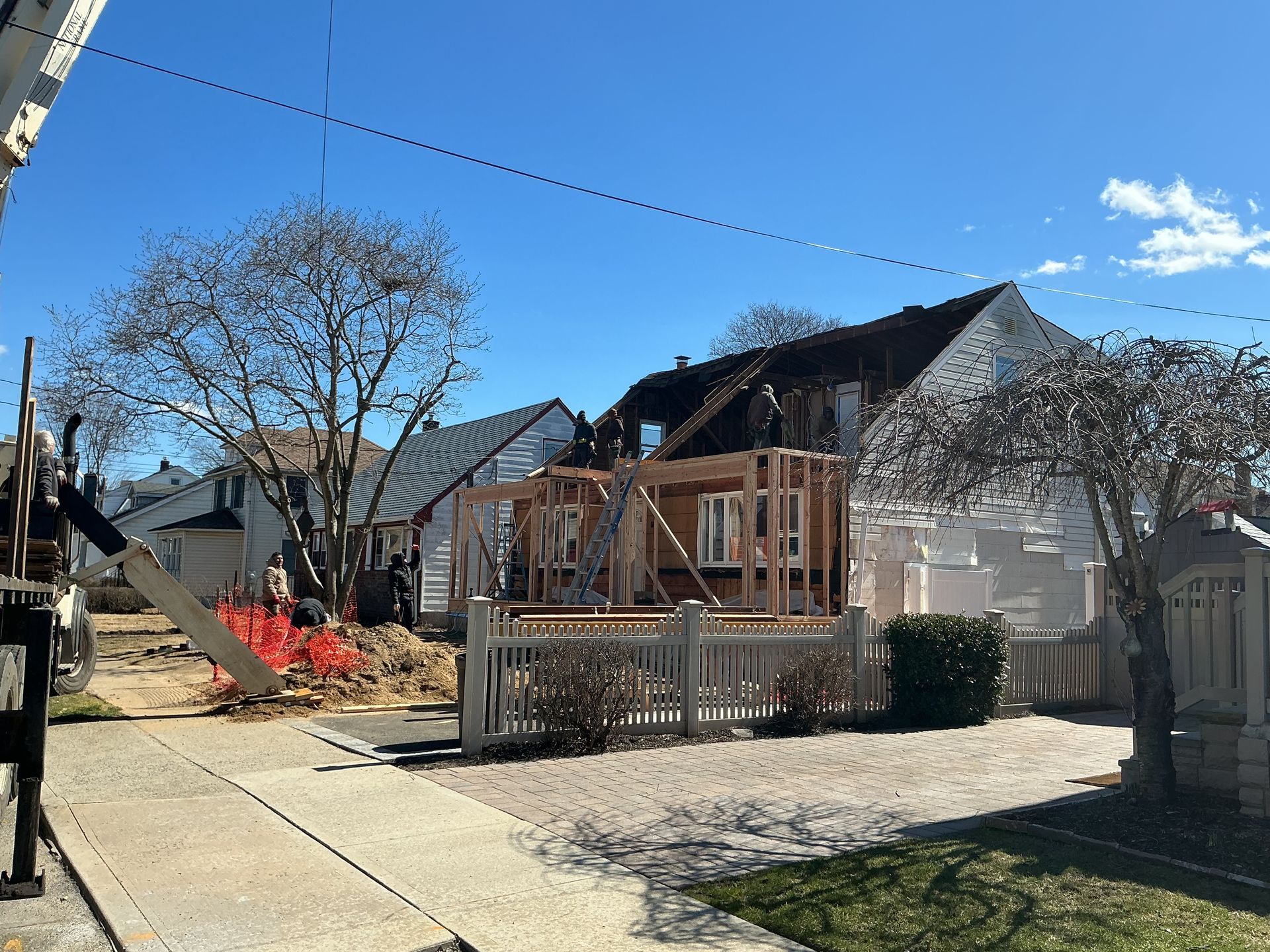 Suburban house under renovation with exposed framing, construction materials, and a driveway in front.