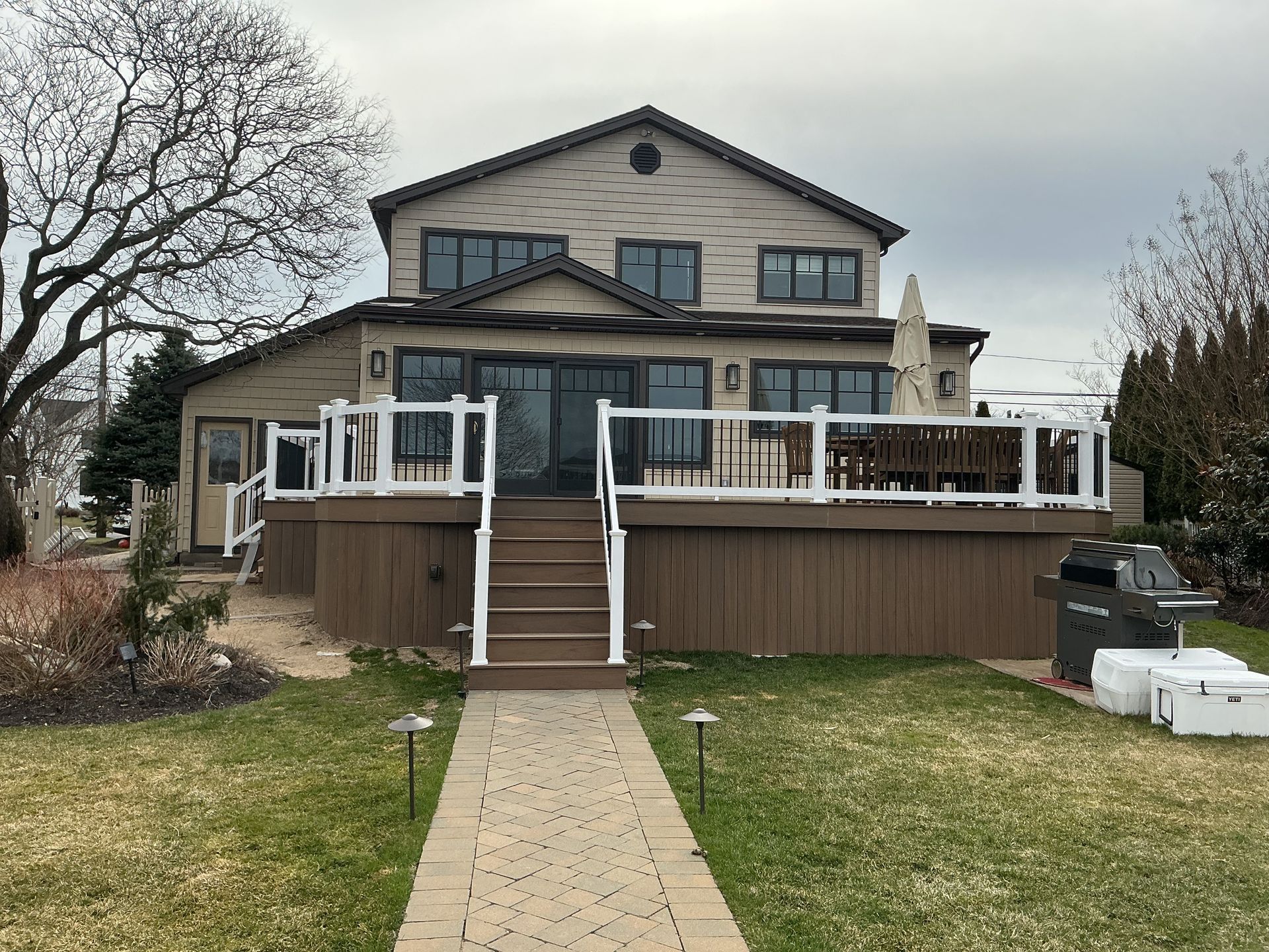 Two-story house with a large wooden deck and stairs, viewed from a front walkway and lawn.
