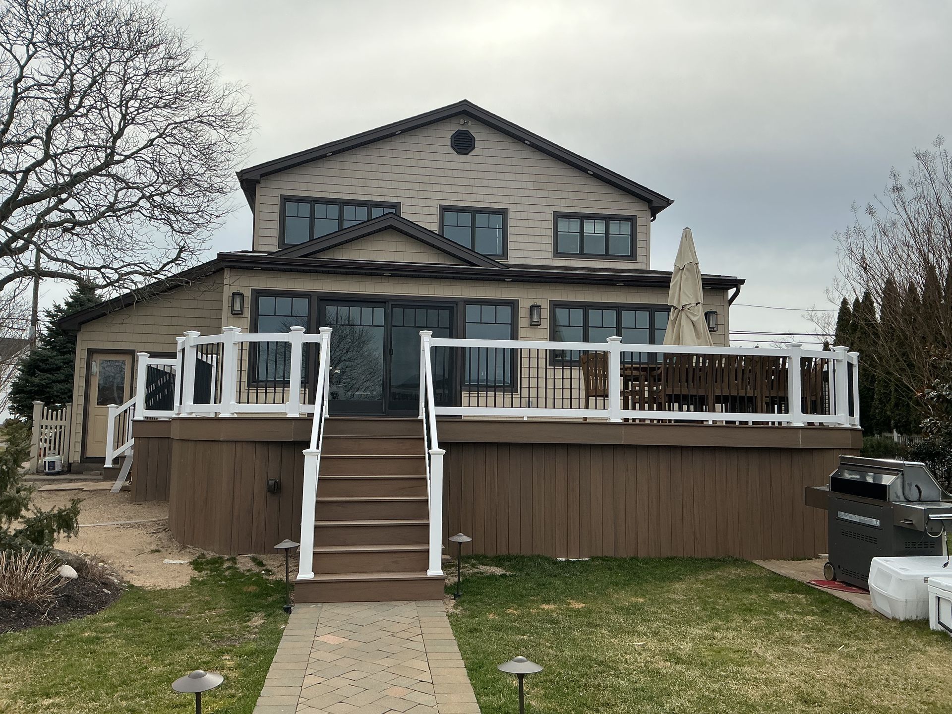 House with a raised wooden deck and white railings in a grassy yard under a cloudy sky