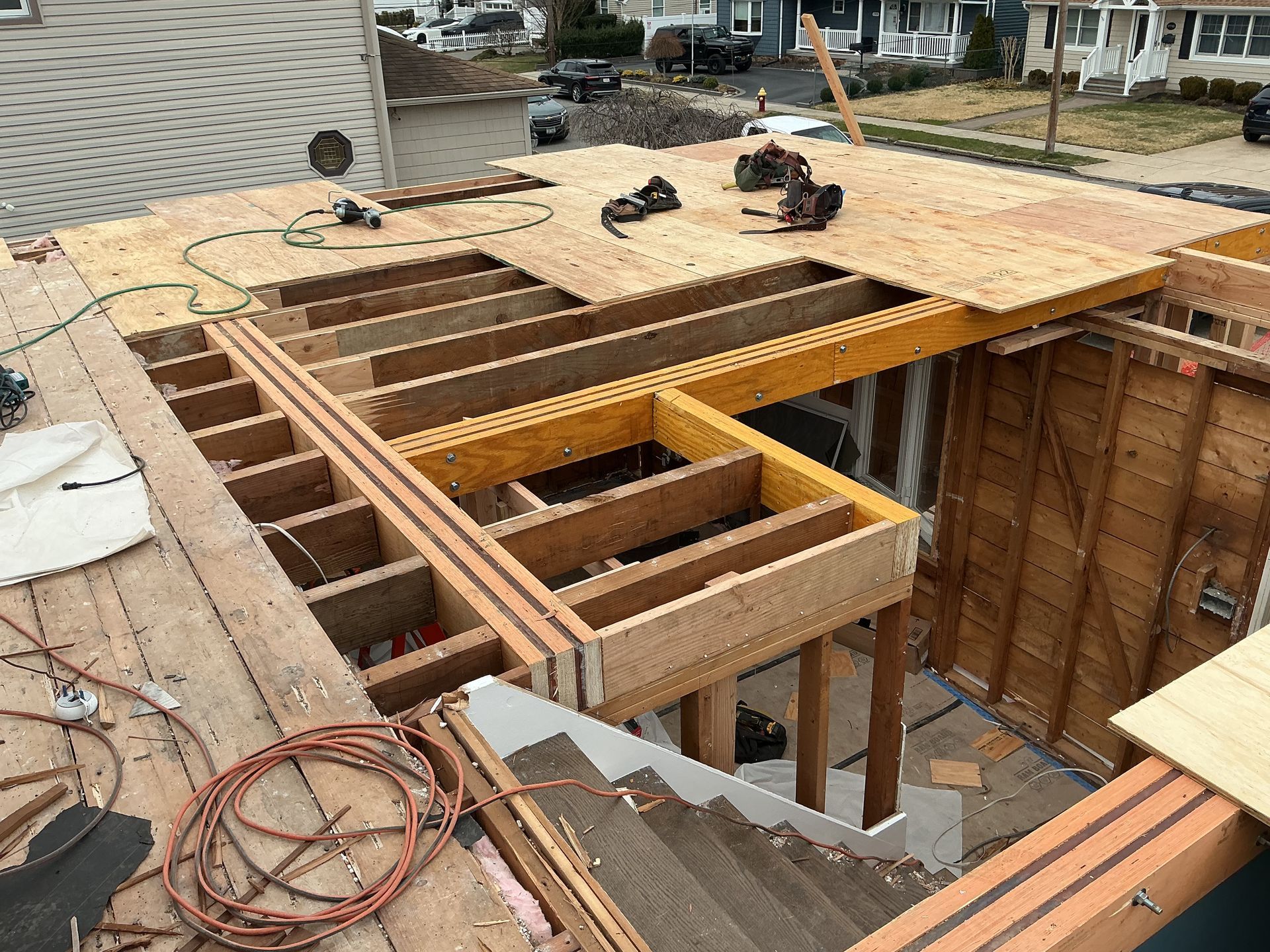 Roof framing under construction with exposed wooden joists, plywood decking, and power tools on top.