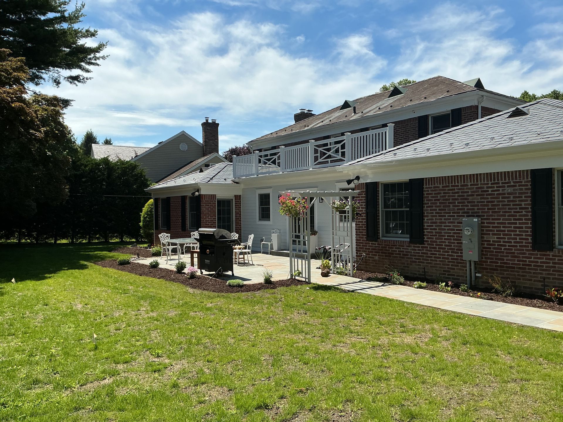 Sunlit backyard patio beside a brick house with outdoor furniture and a green lawn
