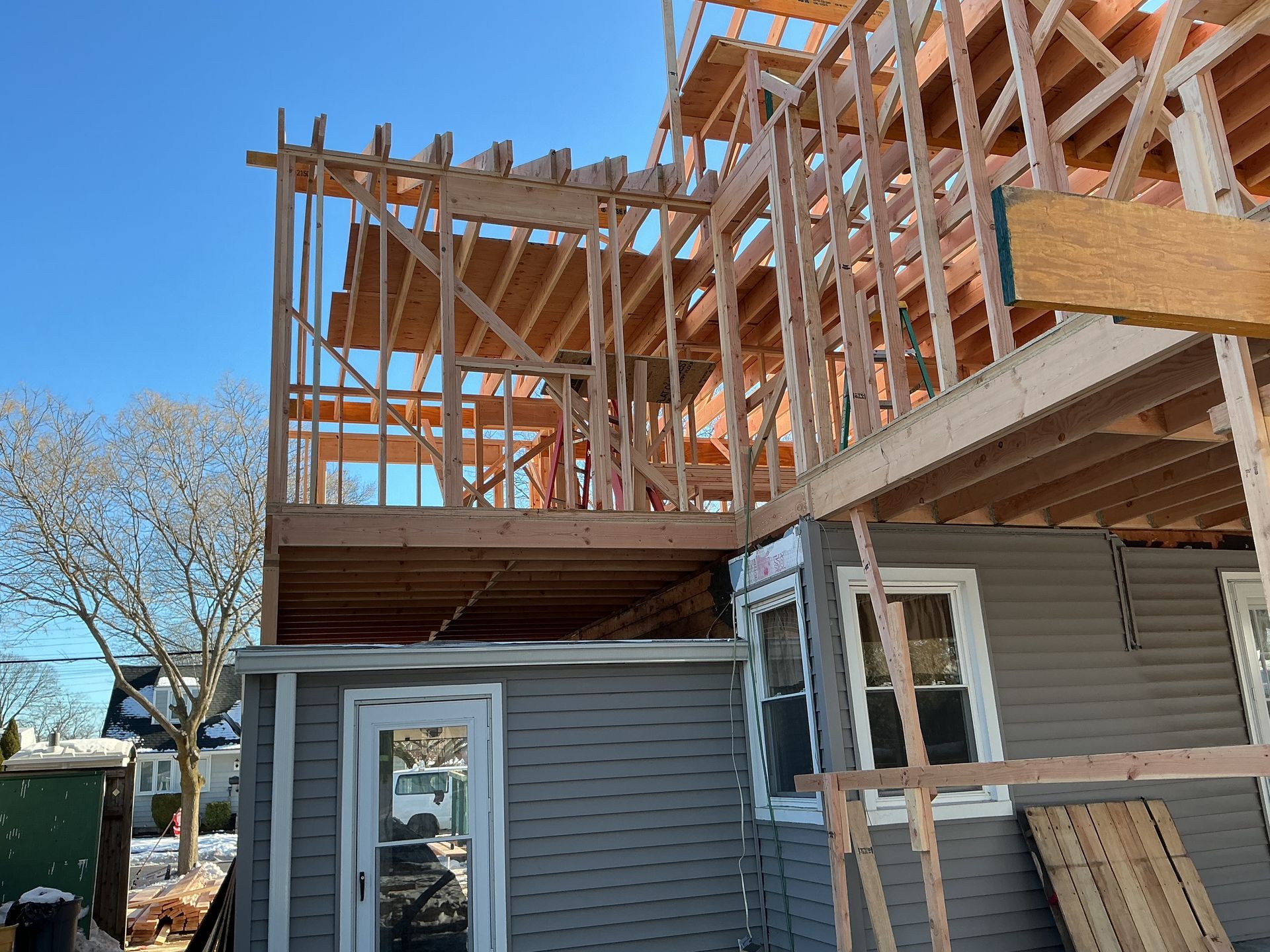 Partially built house with exposed wooden framing and gray siding under a clear blue sky