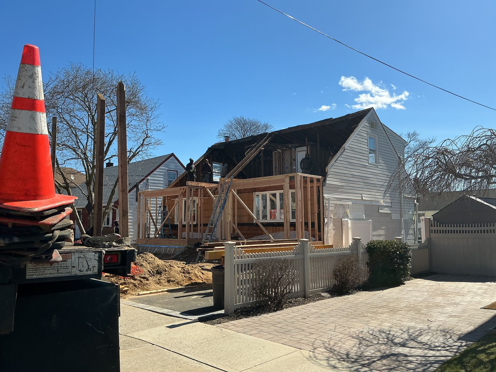 House under renovation with wooden porch framing, orange traffic cone in foreground, under blue sky