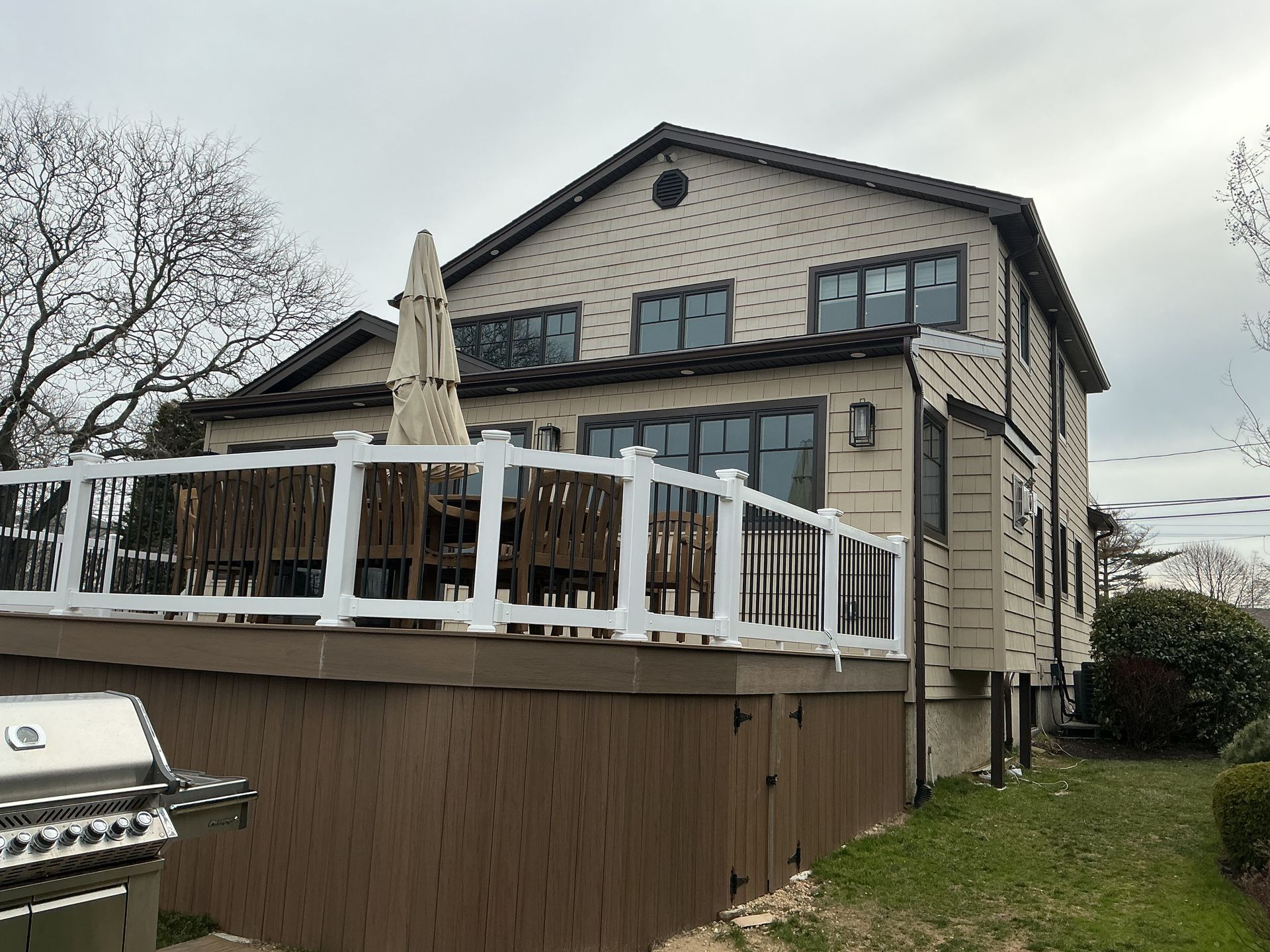 Backyard deck with white railing beside a beige two-story house on a cloudy day