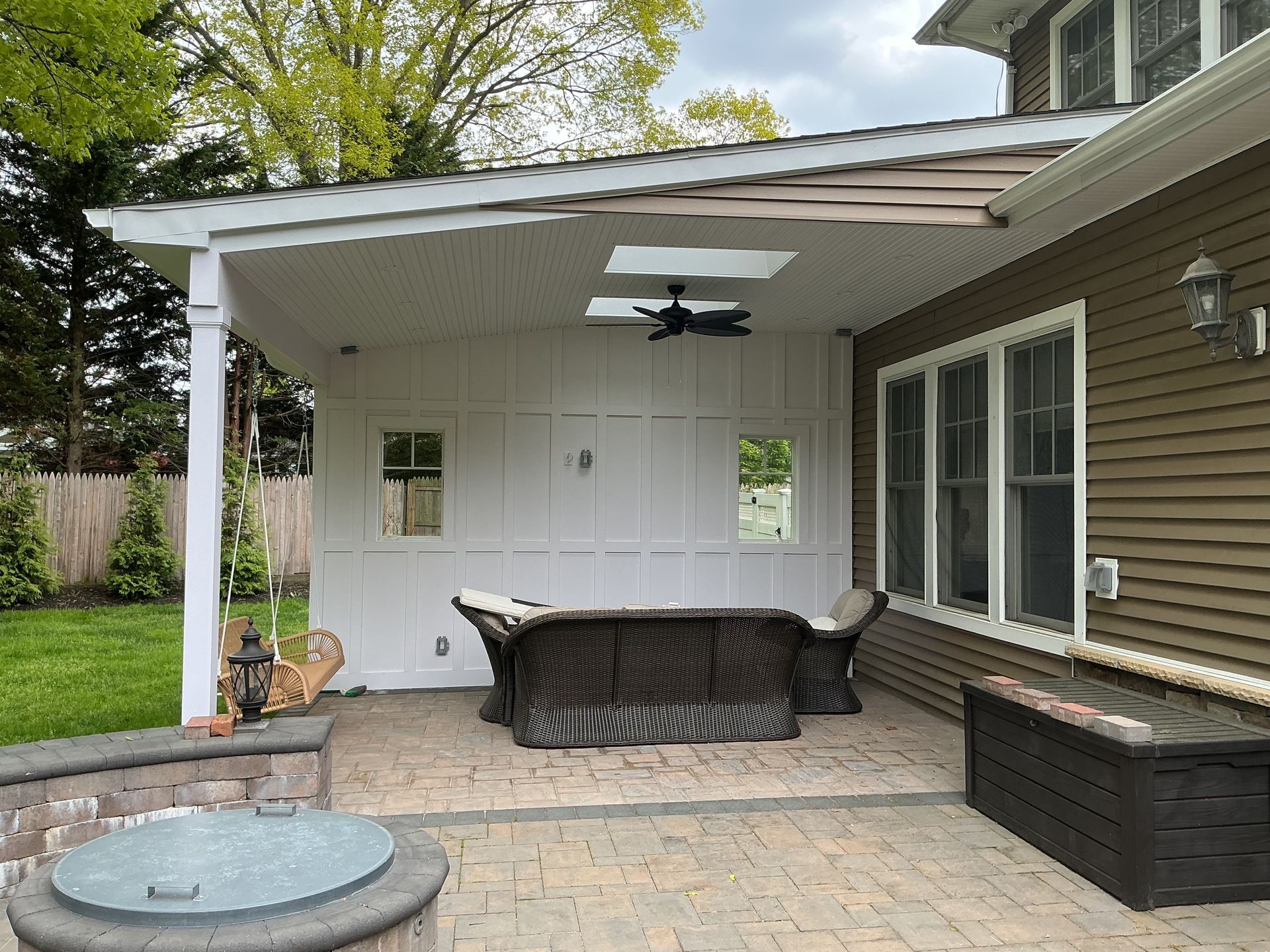 Covered patio with white ceiling fan, wicker dining set, and brown storage bench beside sliding glass doors.