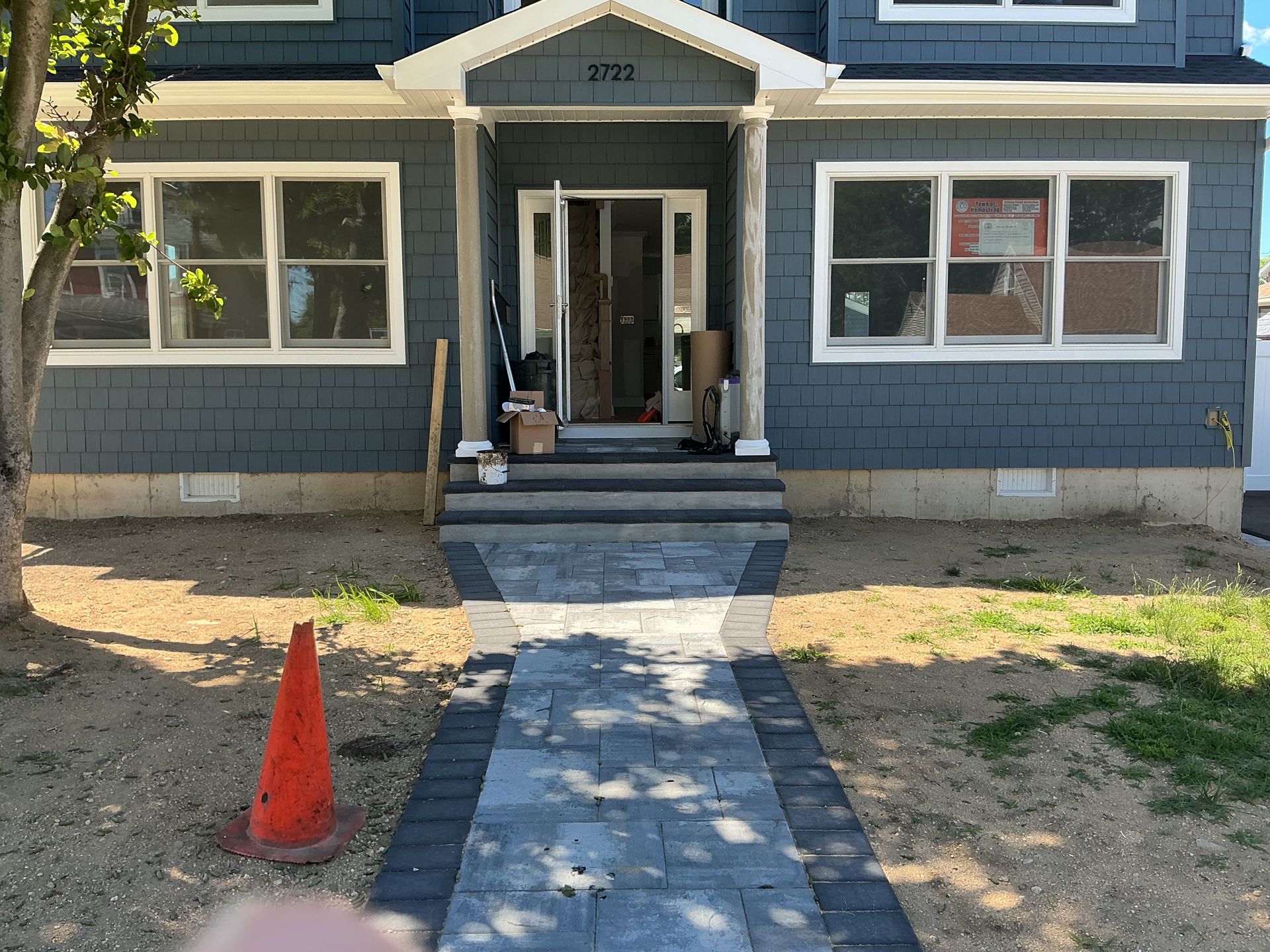 Front porch of a blue house with a central walkway, steps, and an orange traffic cone nearby.